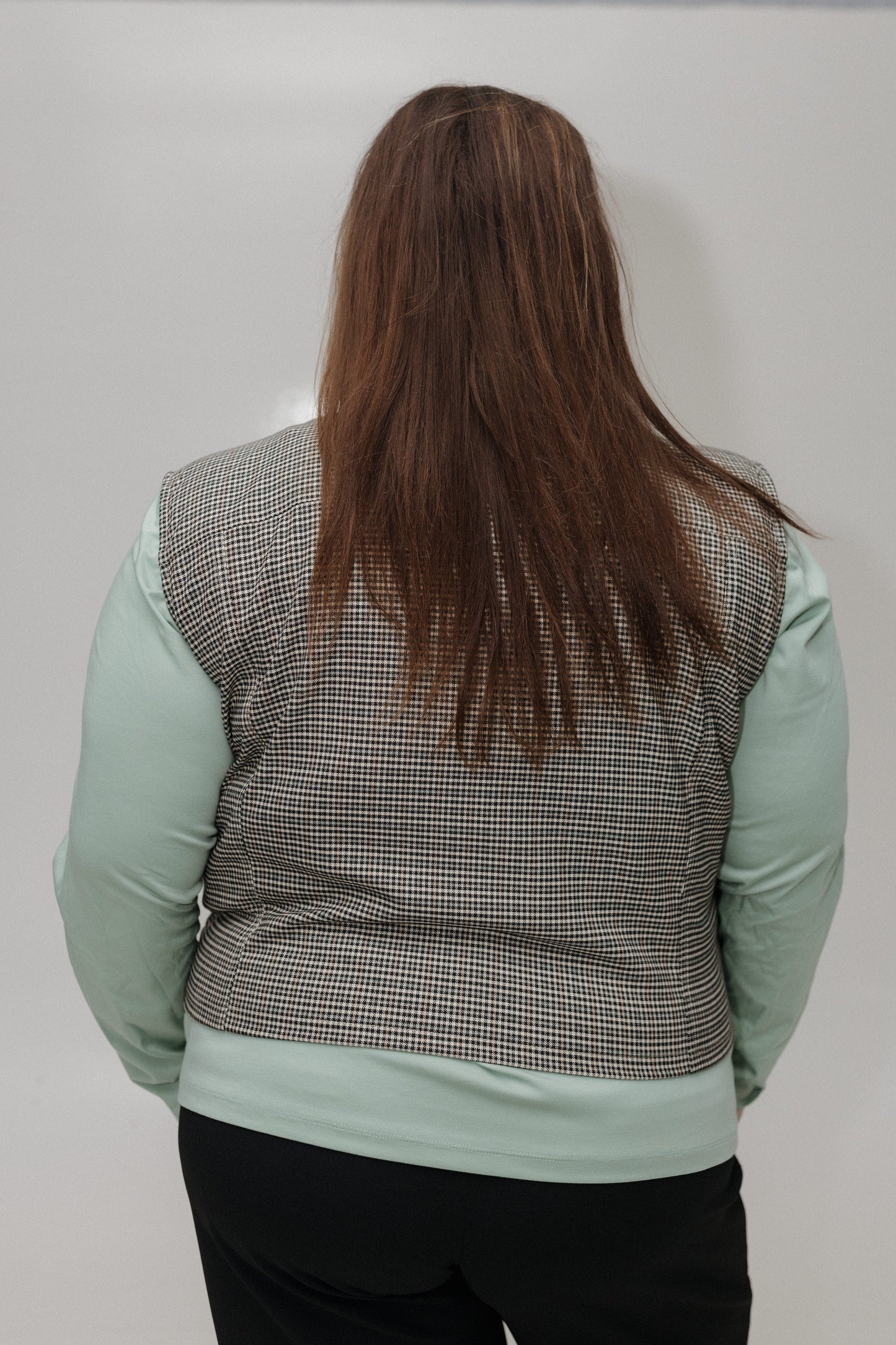 Person wearing a checkered vest over a light green shirt on a plain background