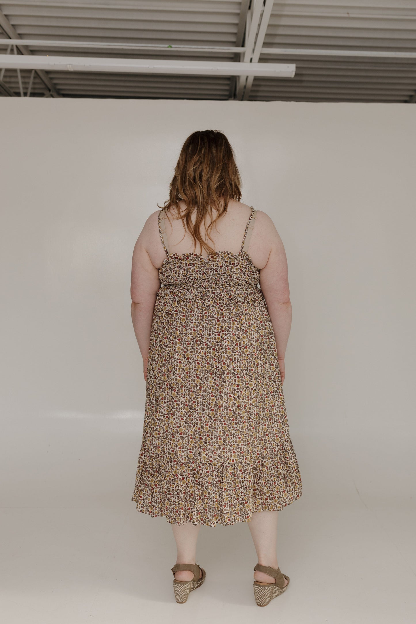 Woman wearing a patterned dress standing against a plain white wall.
