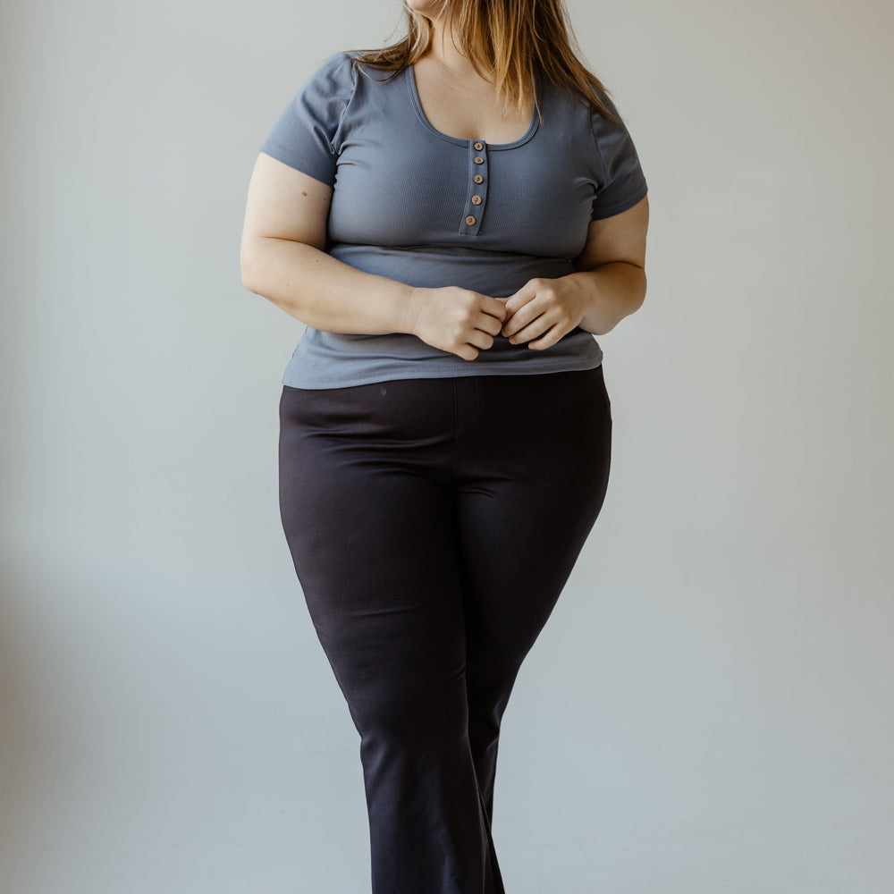 A person stands smiling, wearing a Yesta FLARE TREGGING IN NAVY and ultra-flattering black pants, against a plain background.