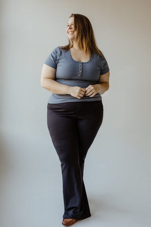 A person stands smiling, wearing a Yesta FLARE TREGGING IN NAVY and ultra-flattering black pants, against a plain background.