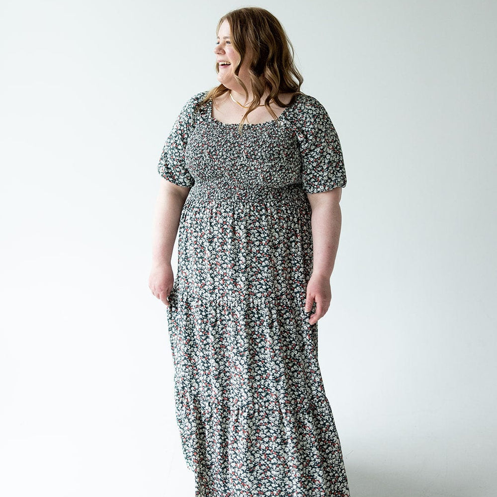 A person wearing a floral-patterned dress with bubble sleeves stands on a light background, looking to the side and smiling.