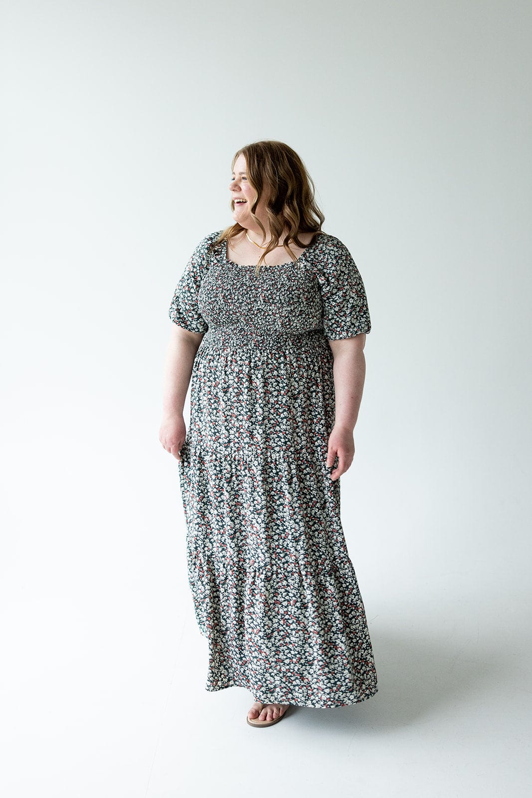 A person wearing a floral-patterned dress with bubble sleeves stands on a light background, looking to the side and smiling.