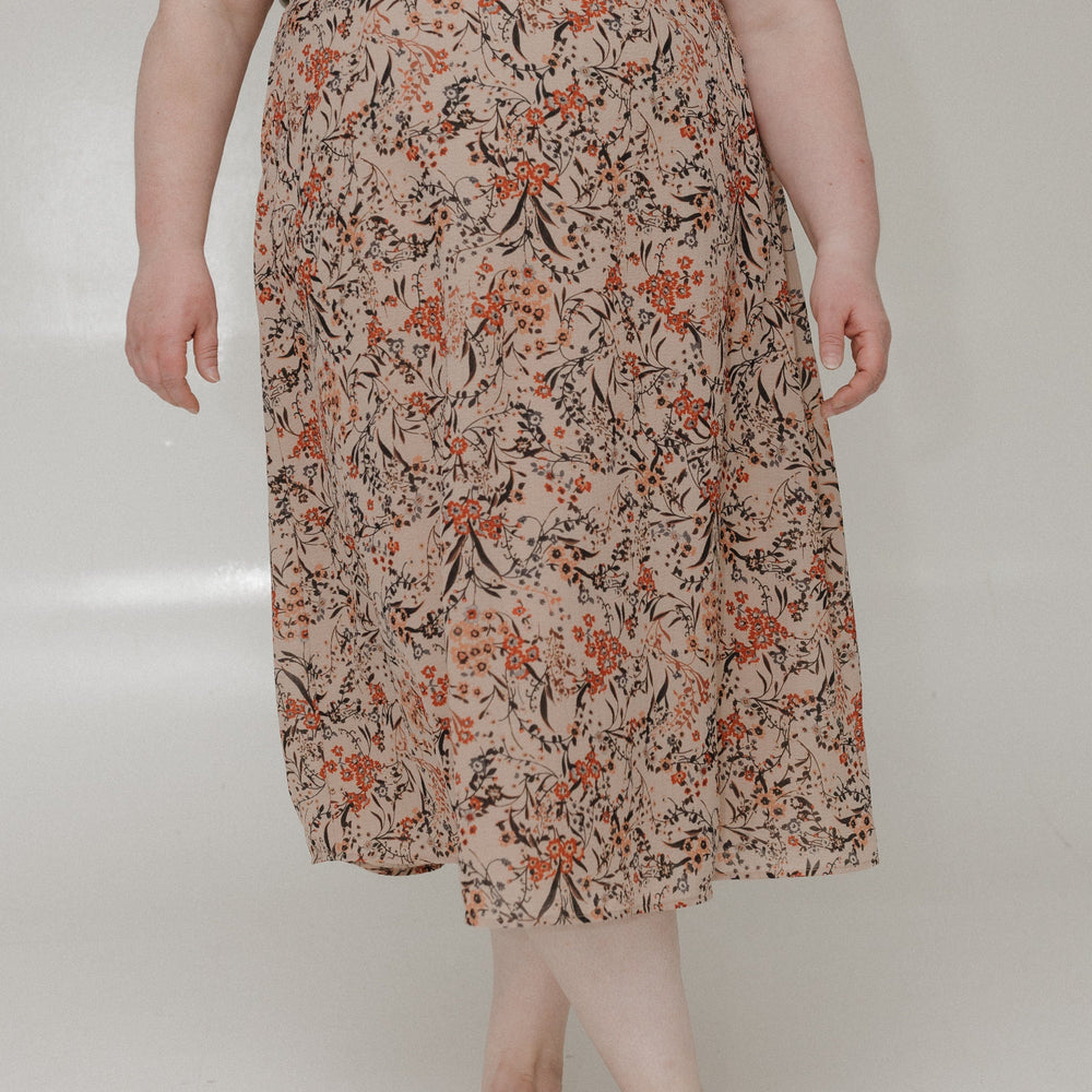 Person wearing a floral skirt and brown top on a plain background