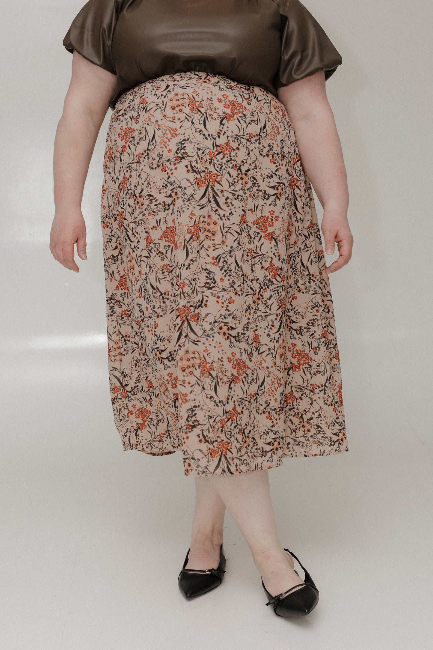 Person wearing a floral skirt and brown top on a plain background
