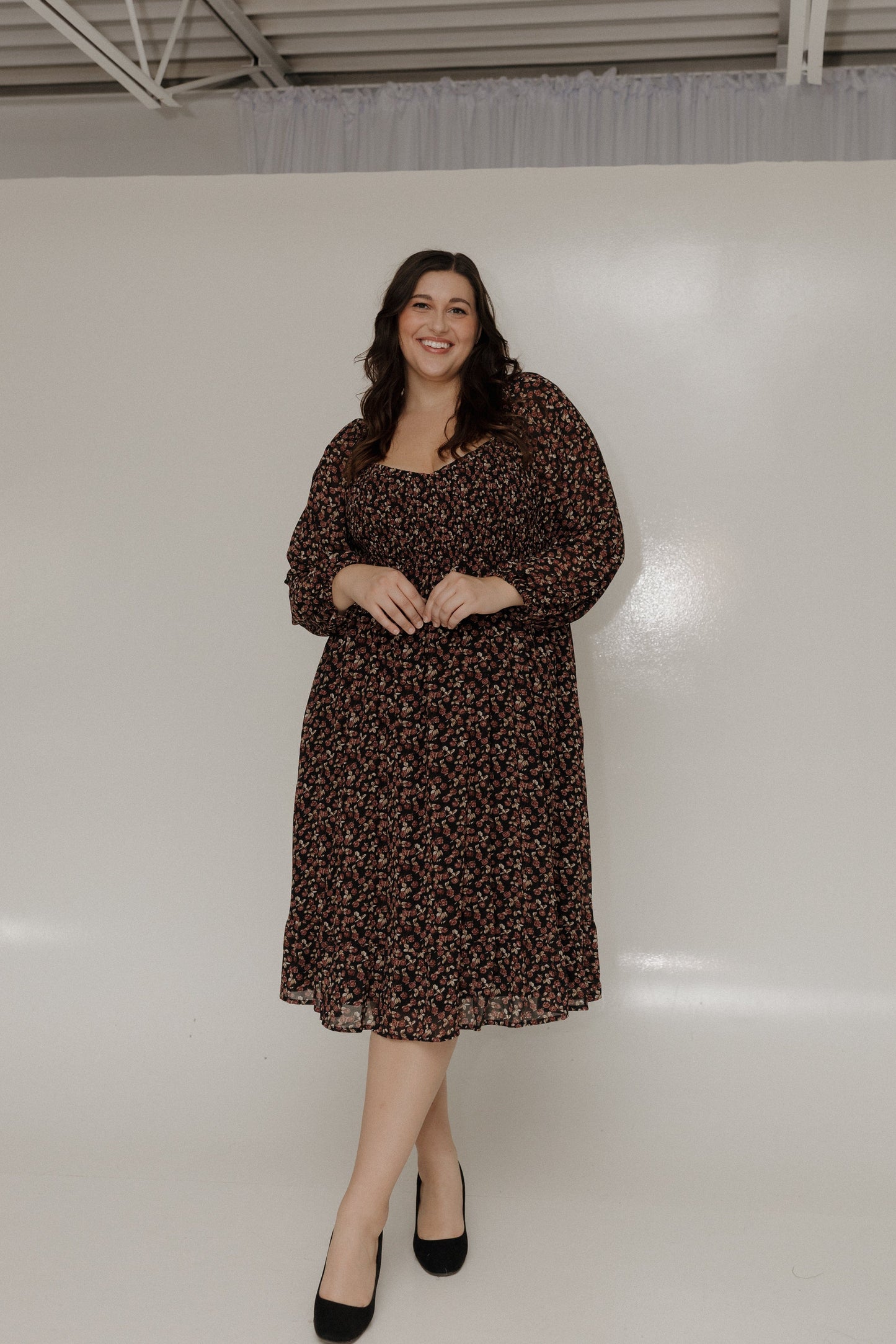 Woman wearing a brown floral dress standing against a white wall