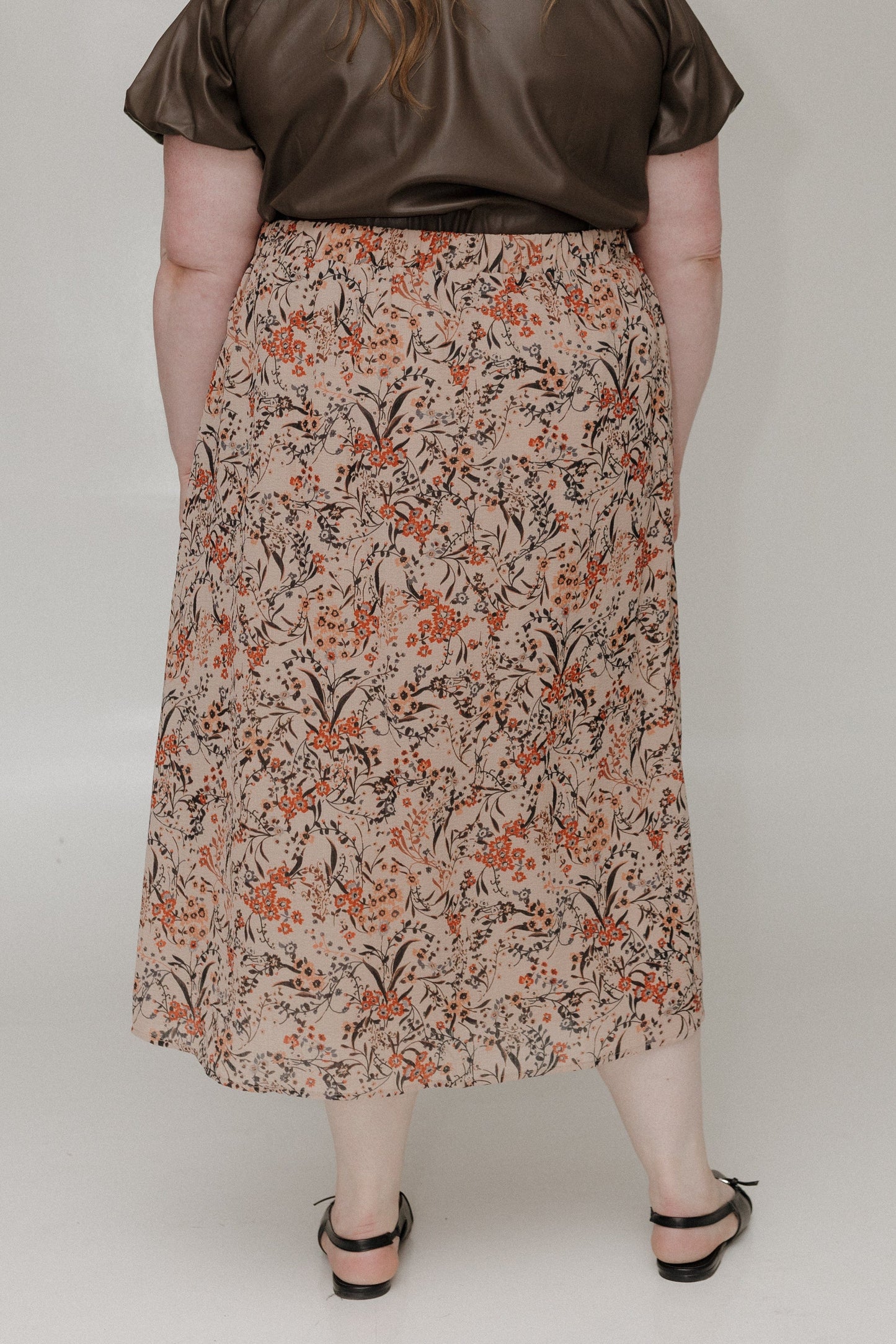 Person wearing a floral skirt and brown top on a plain background