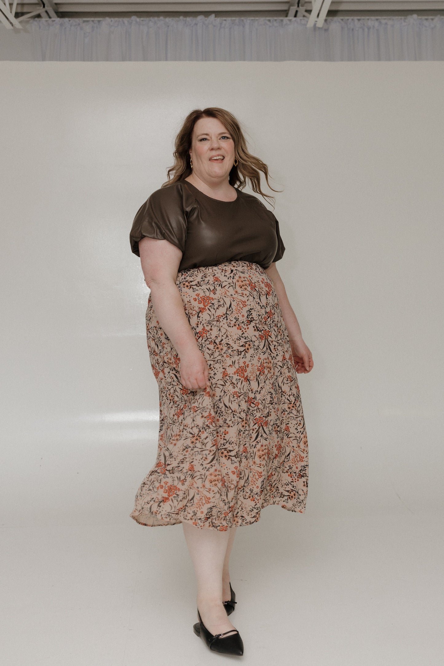 Woman wearing a brown top and floral skirt against a plain background