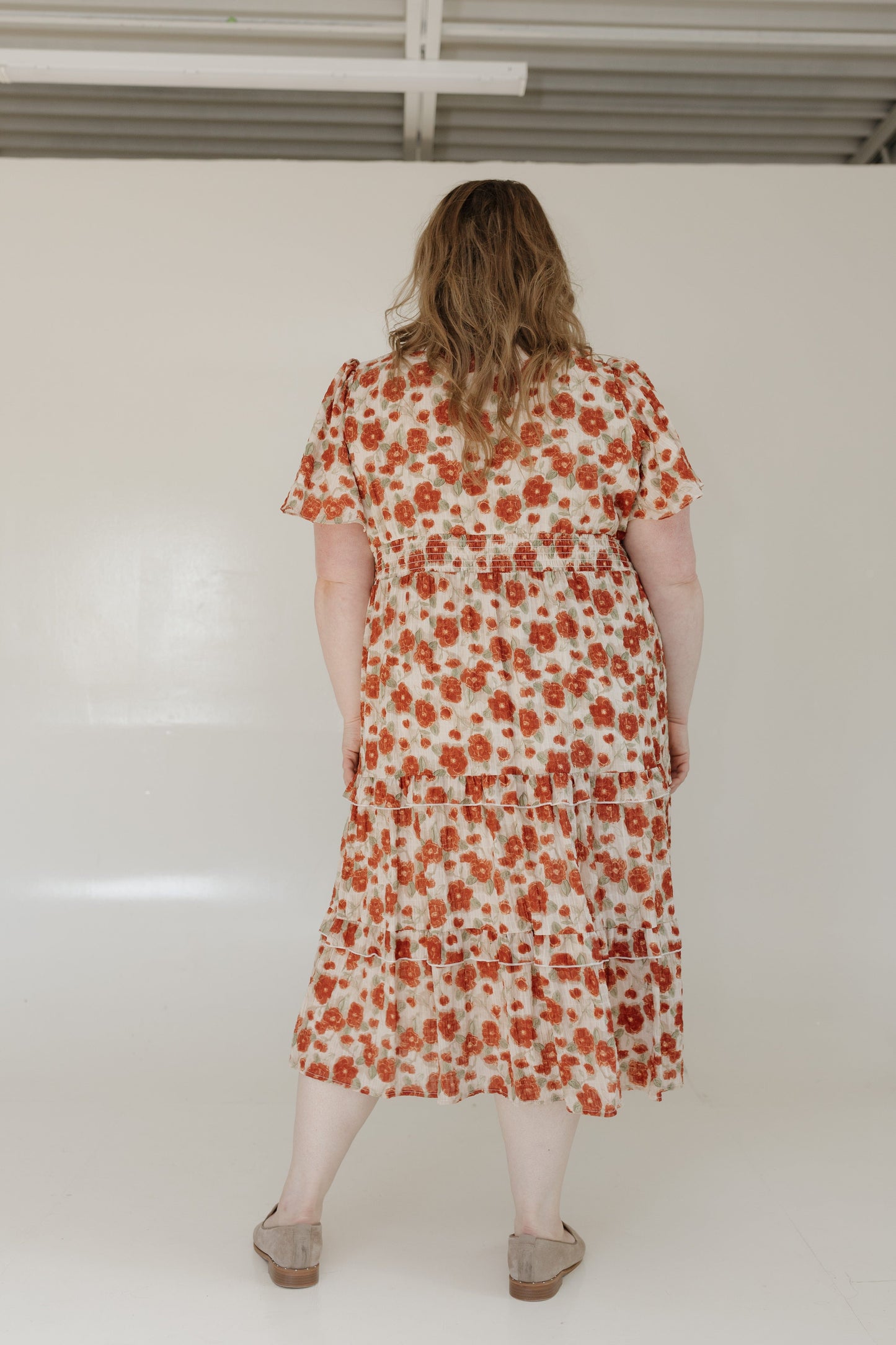 Person wearing a floral dress standing against a white wall