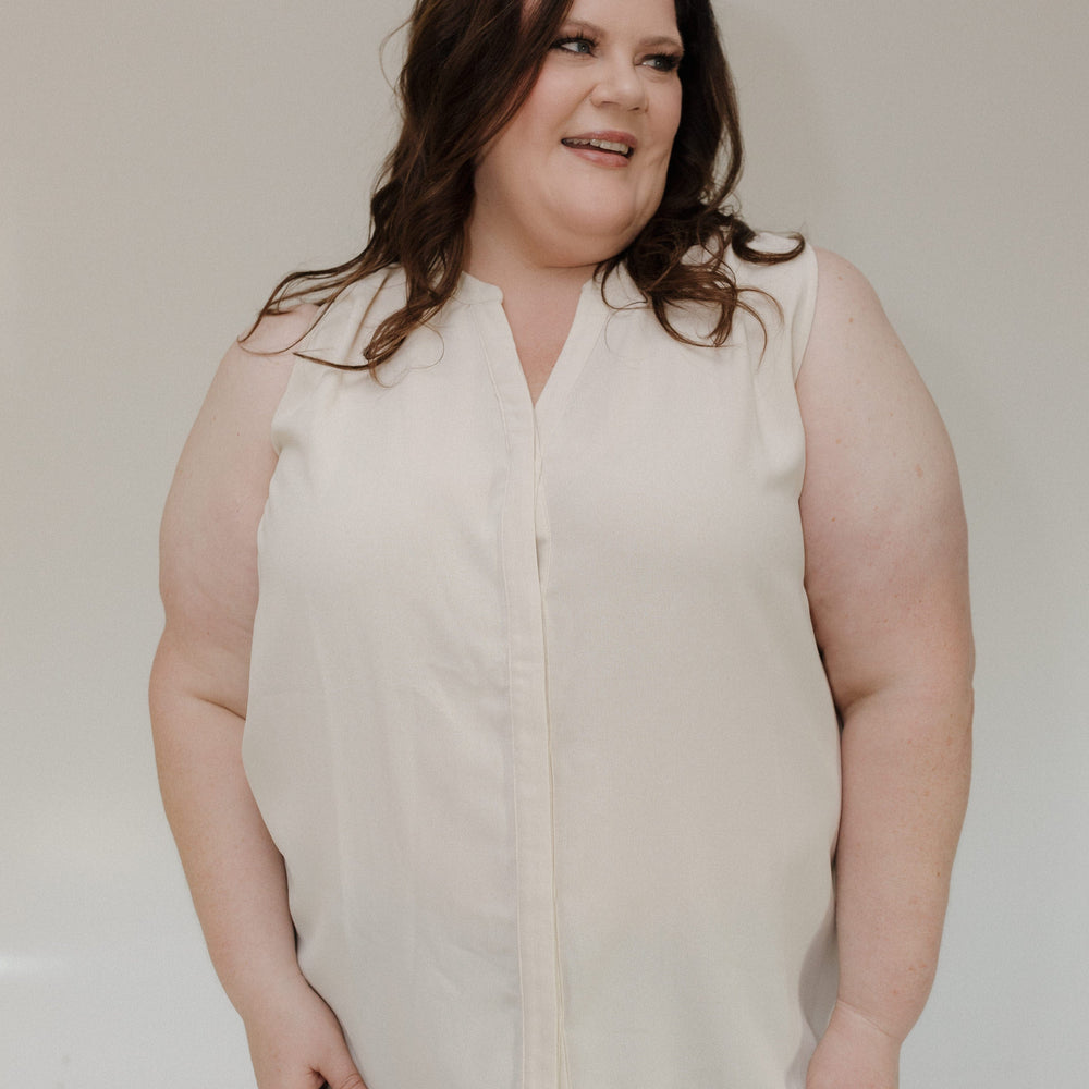 Woman wearing a beige sleeveless blouse against a plain background