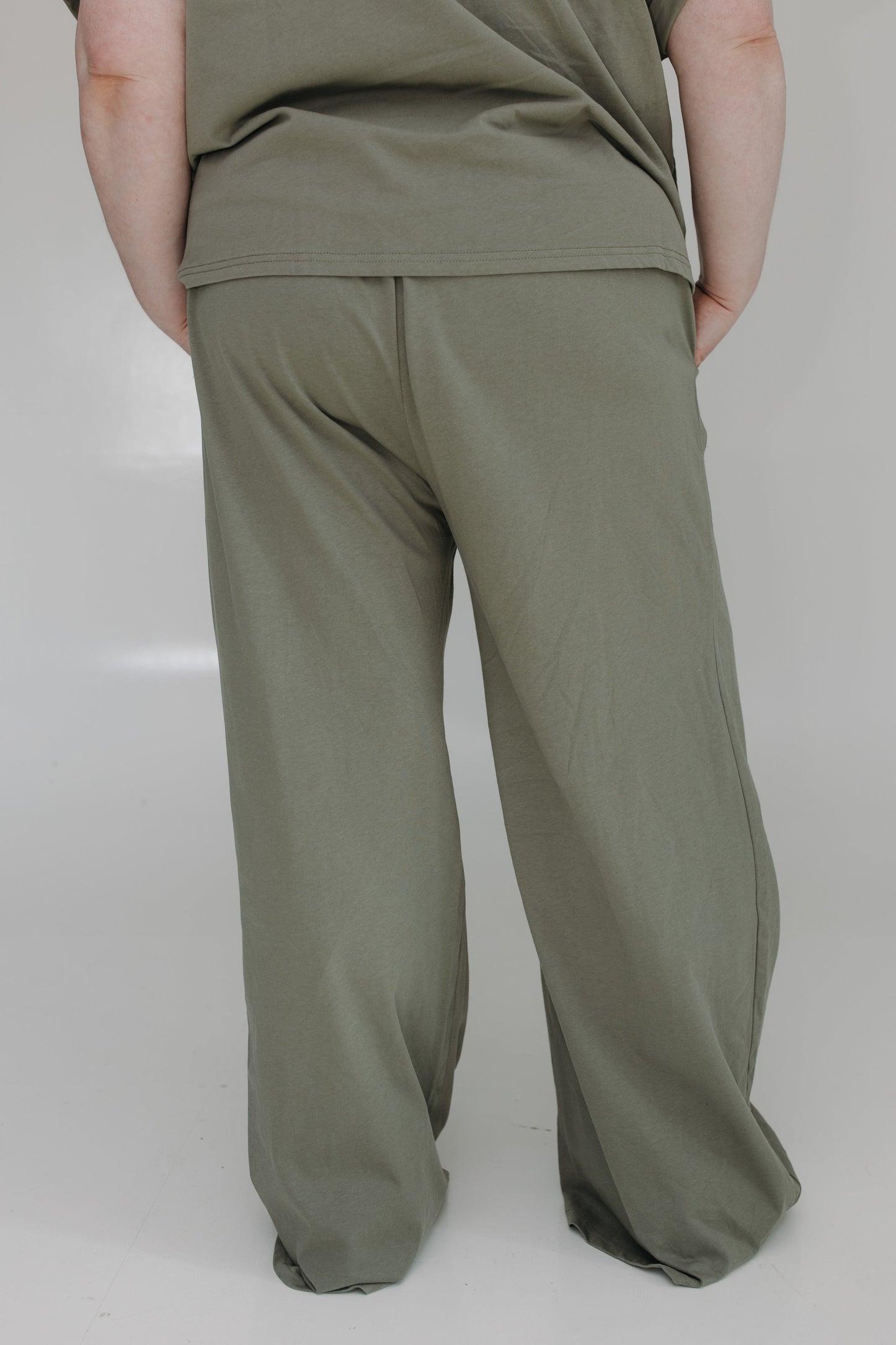 Person wearing olive green pants and a matching top on a plain background