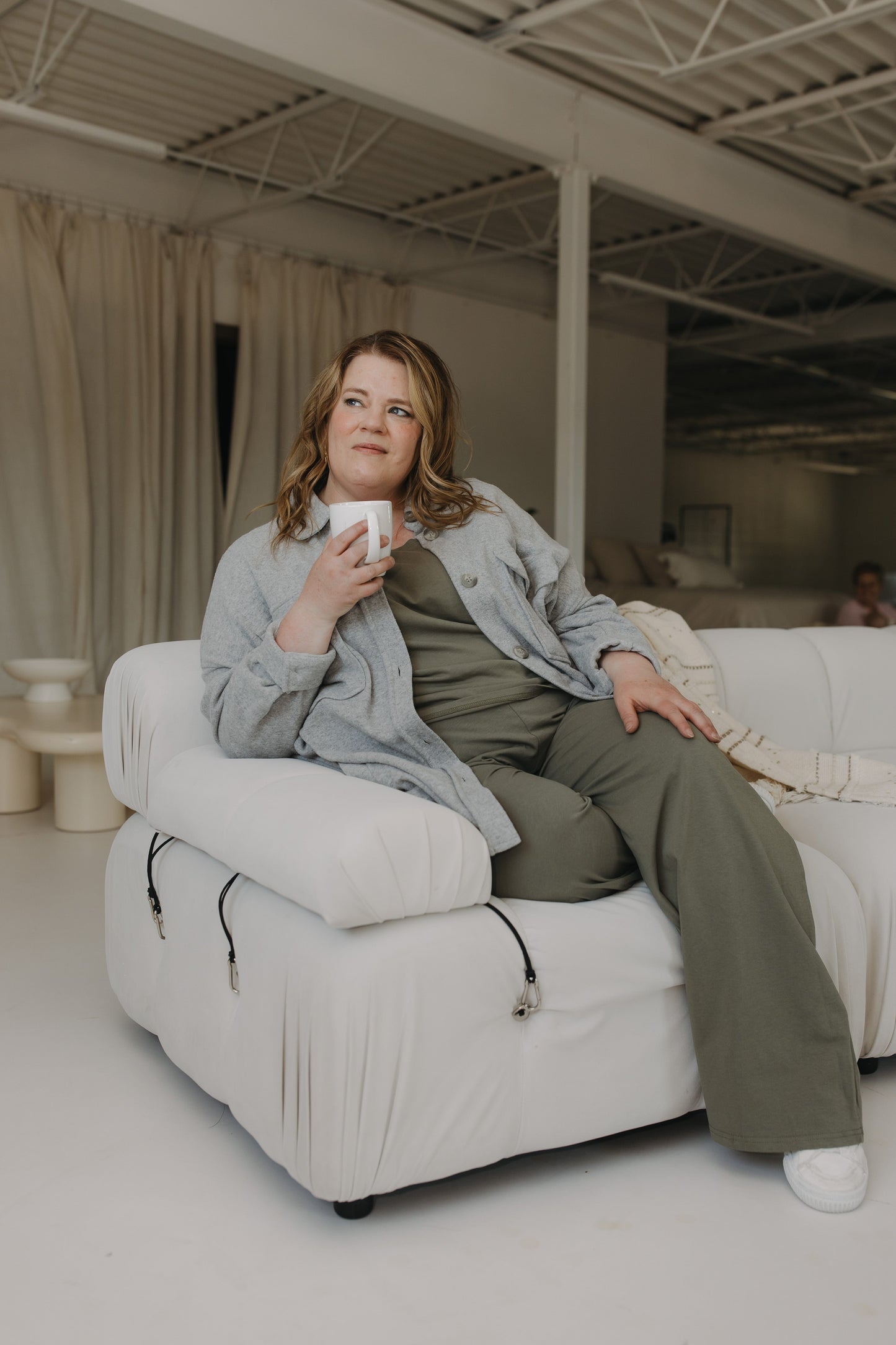 Woman sitting on a white recliner holding a mug in a modern living room.