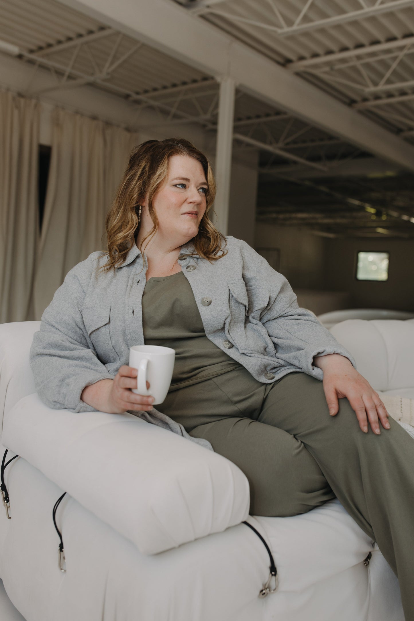 Woman sitting on a white couch holding a mug in an indoor setting