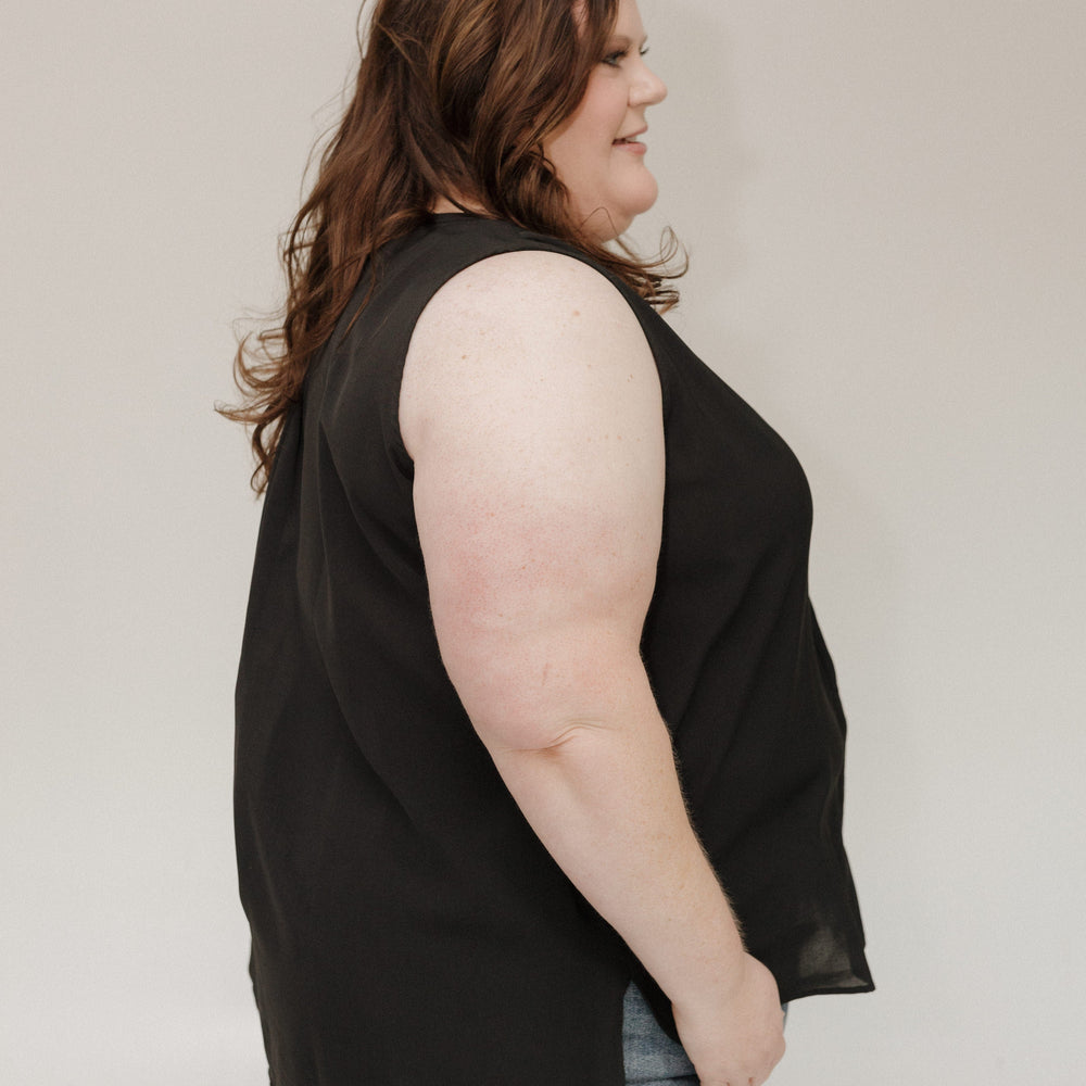Person wearing a black sleeveless top and blue jeans against a plain background