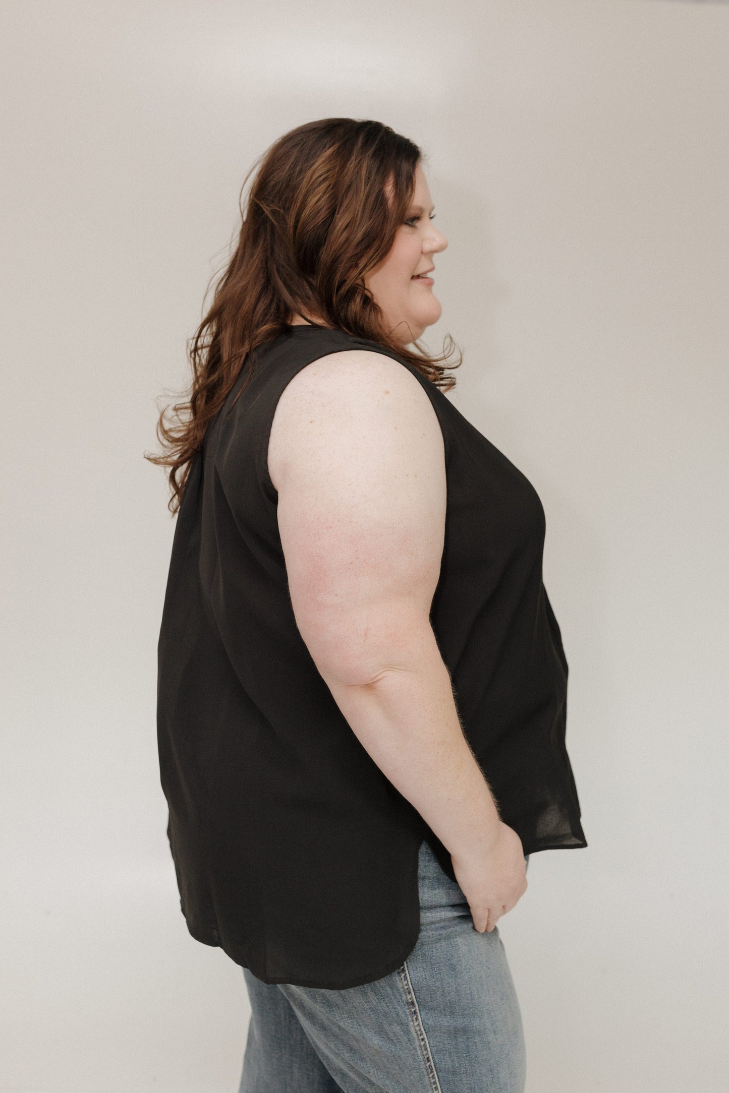 Person wearing a black sleeveless top and blue jeans against a plain background