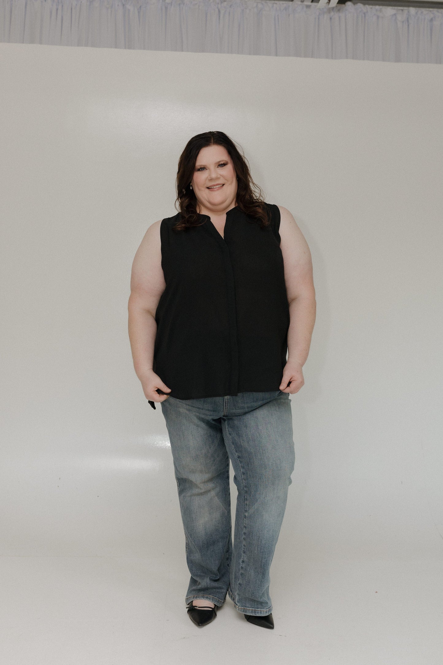 Person wearing a black sleeveless top and blue jeans on a white background