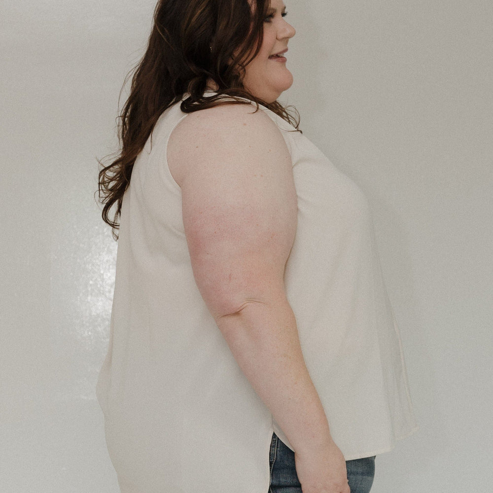 Woman wearing a beige top and blue jeans against a white background