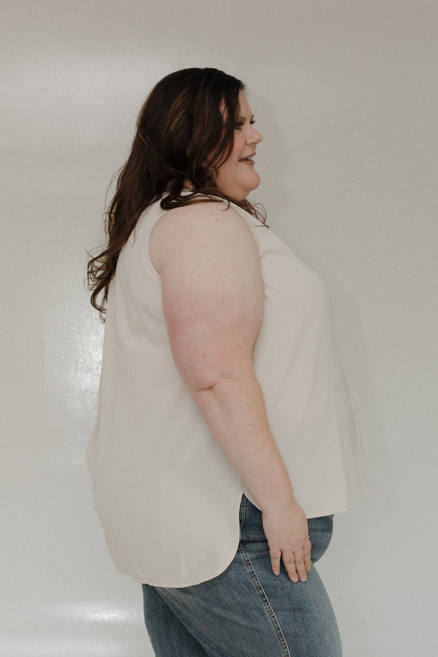Woman wearing a beige top and blue jeans against a white background