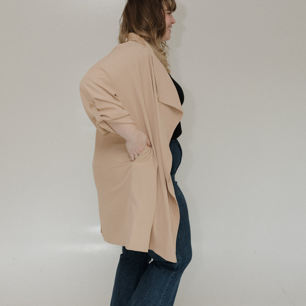 Person wearing a beige coat and blue jeans on a plain background