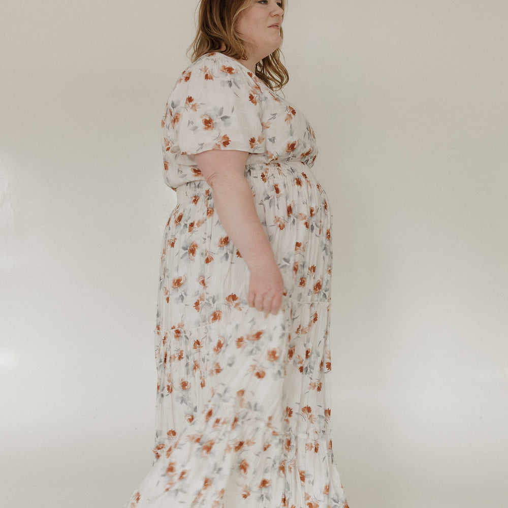 Woman wearing a floral dress standing against a plain background
