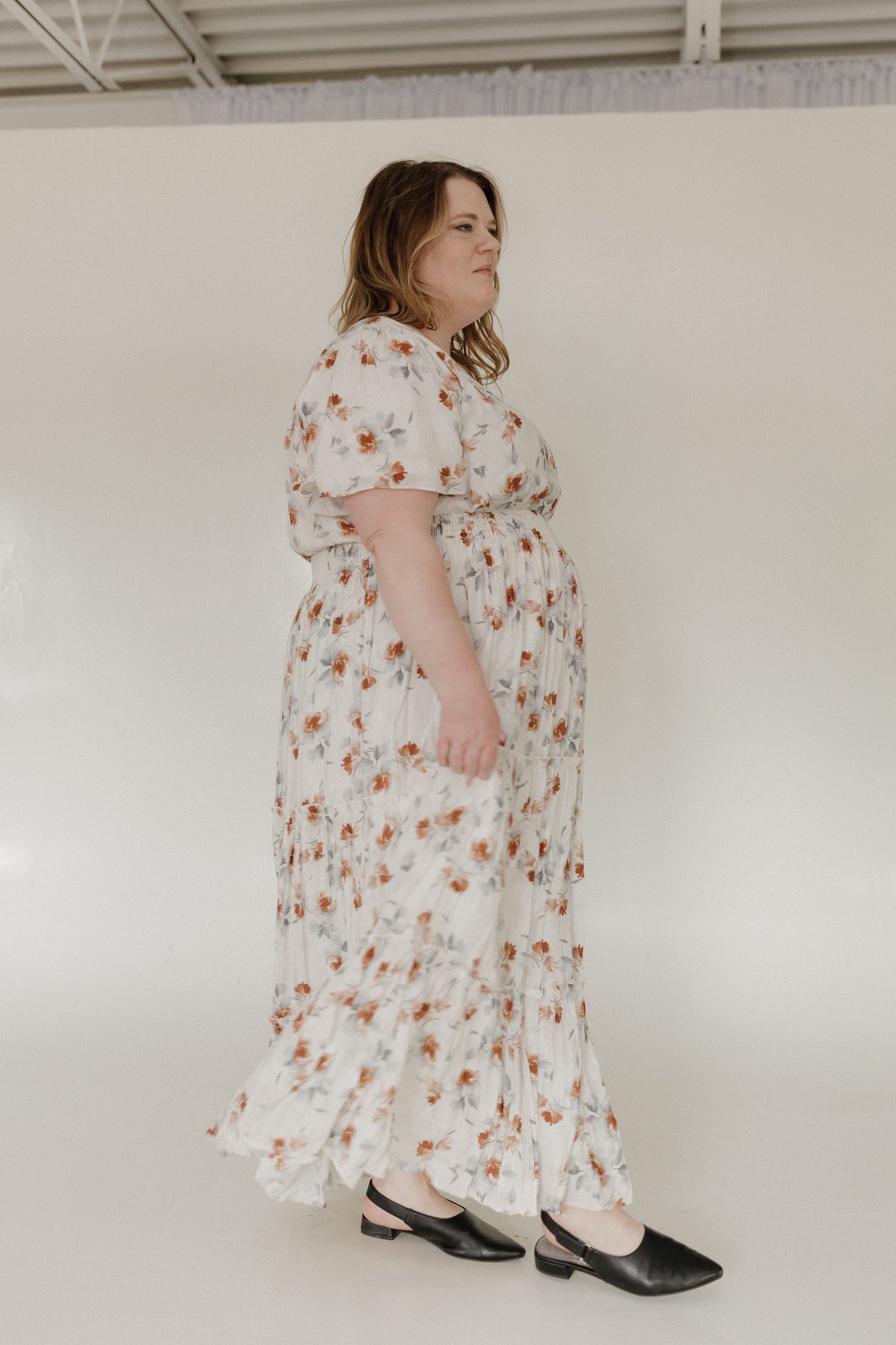 Woman wearing a floral dress standing against a plain background