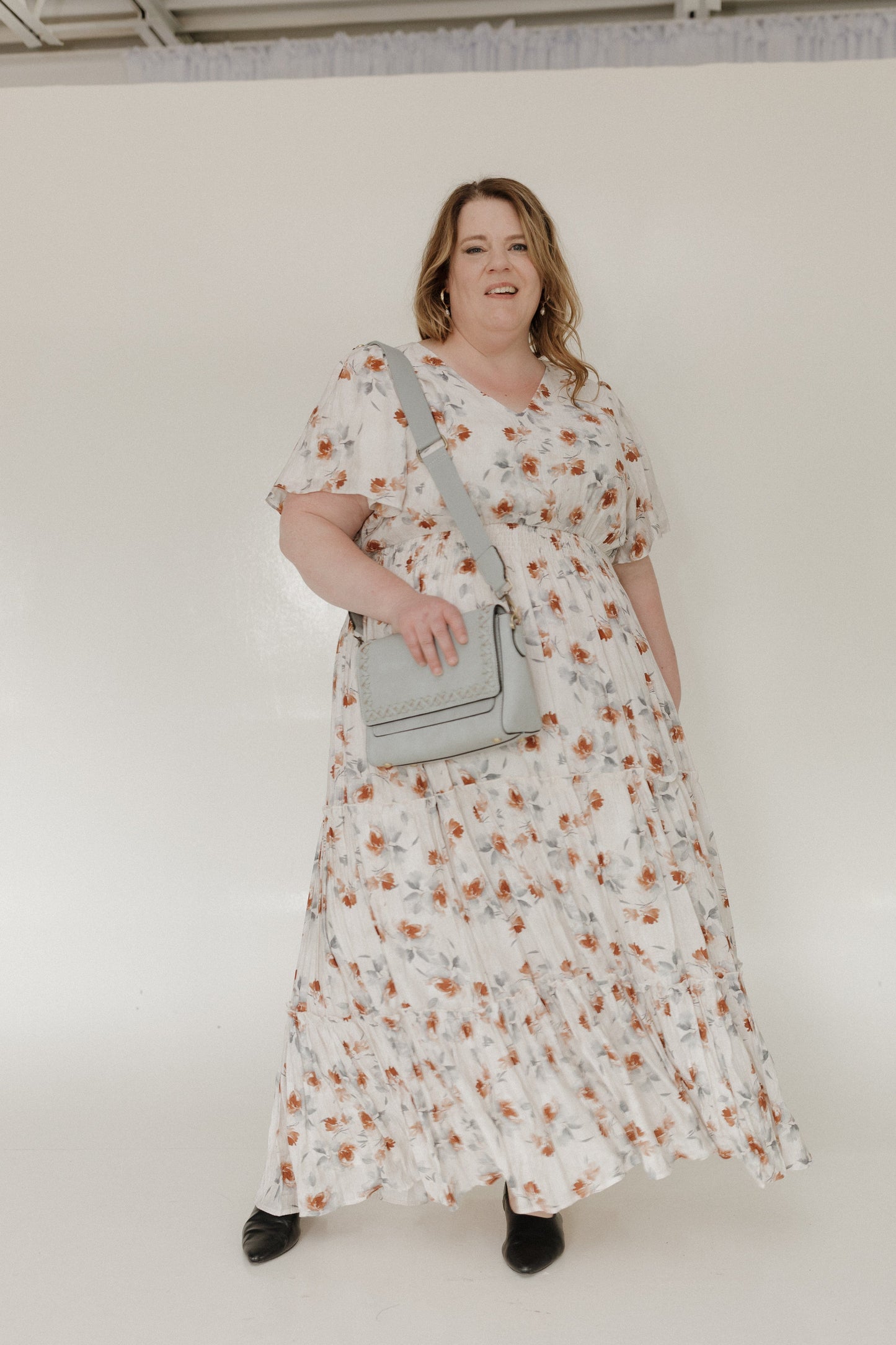 Woman wearing a floral dress holding a gray purse against a white background