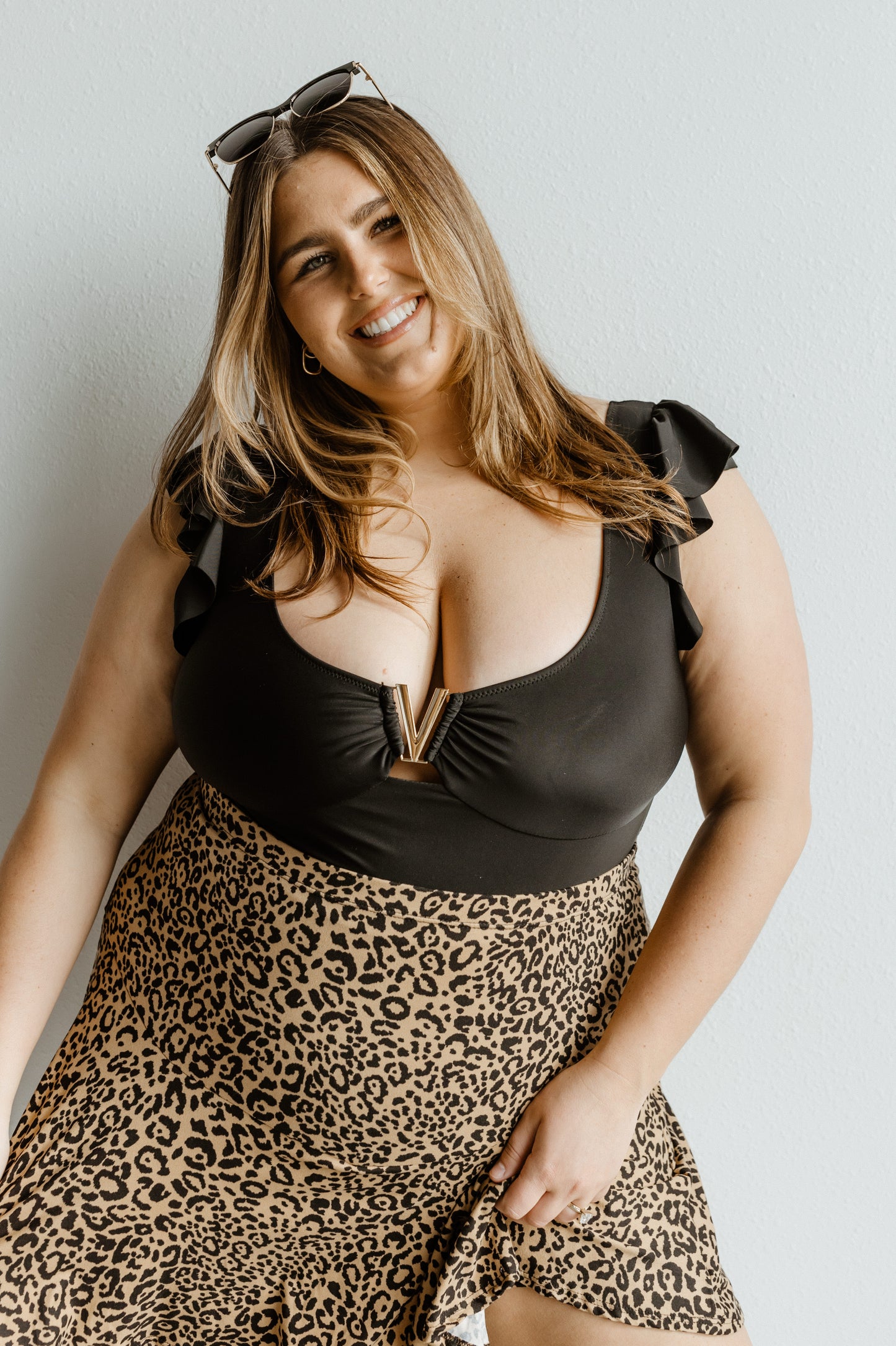 Woman wearing a black top and leopard print skirt against a plain background