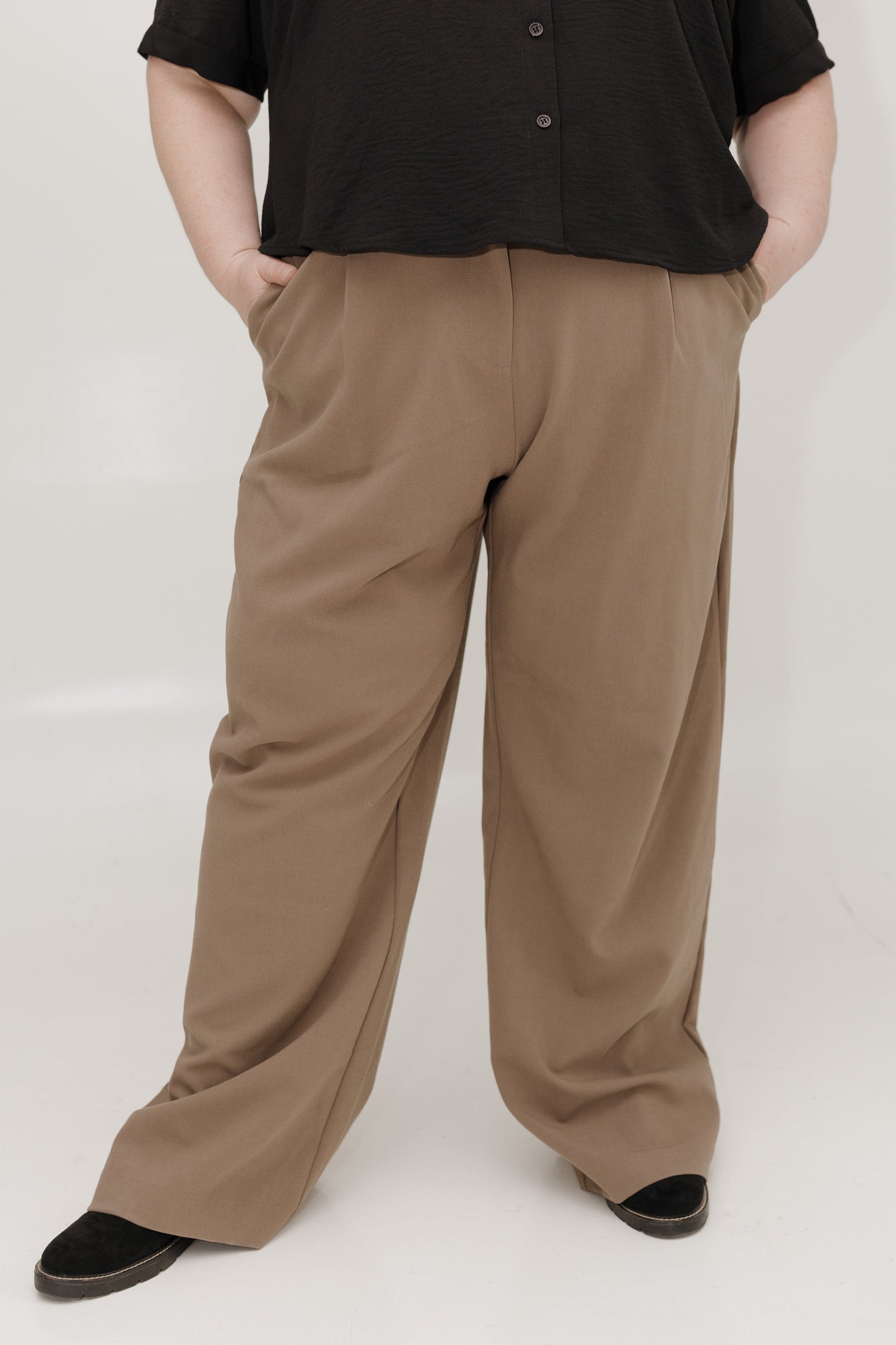 Person wearing brown wide-leg pants and a black top on a white background