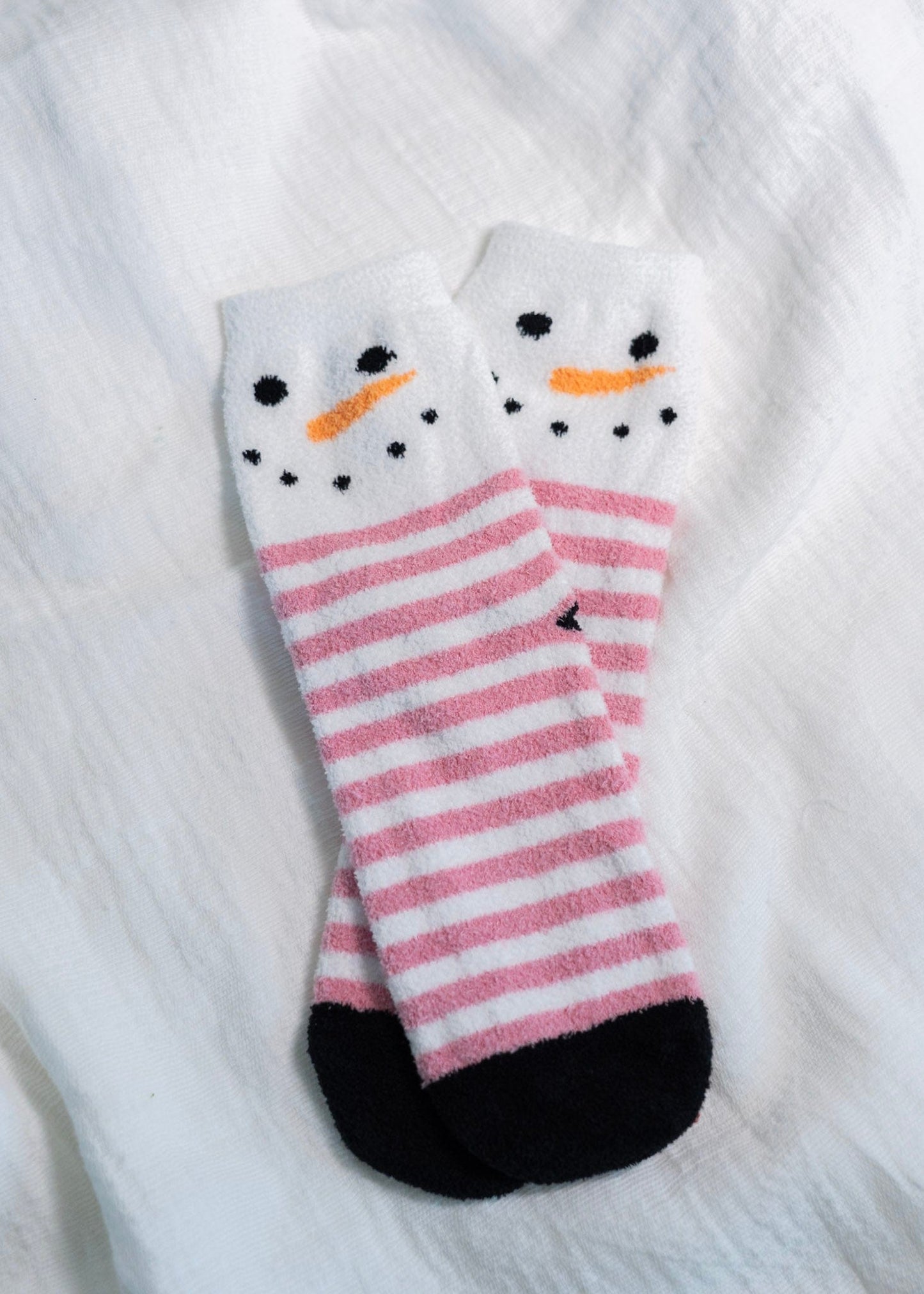 Pink and white striped socks with snowman design on a white textured background