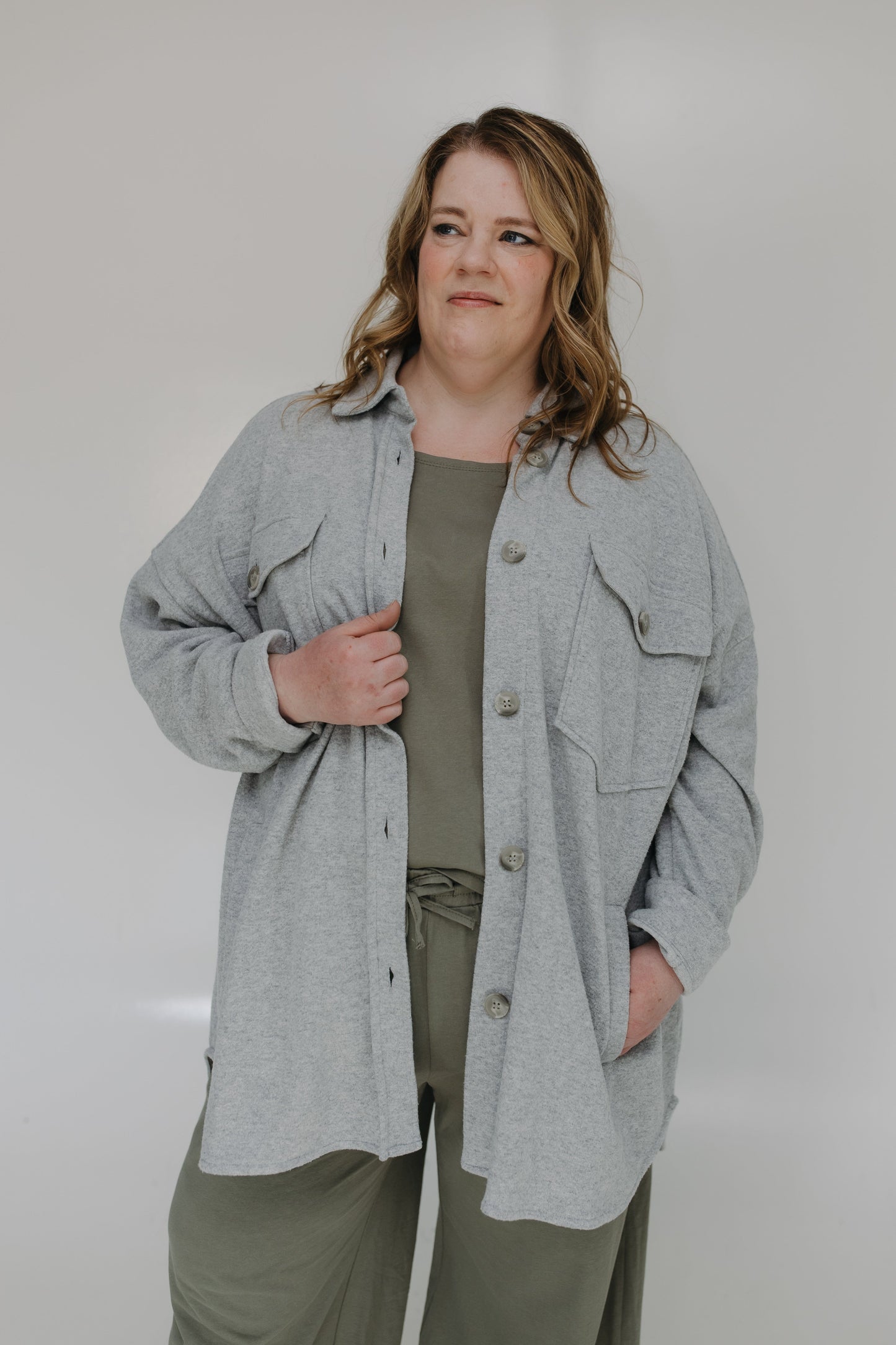 Woman wearing a gray jacket over a green shirt and pants against a white background