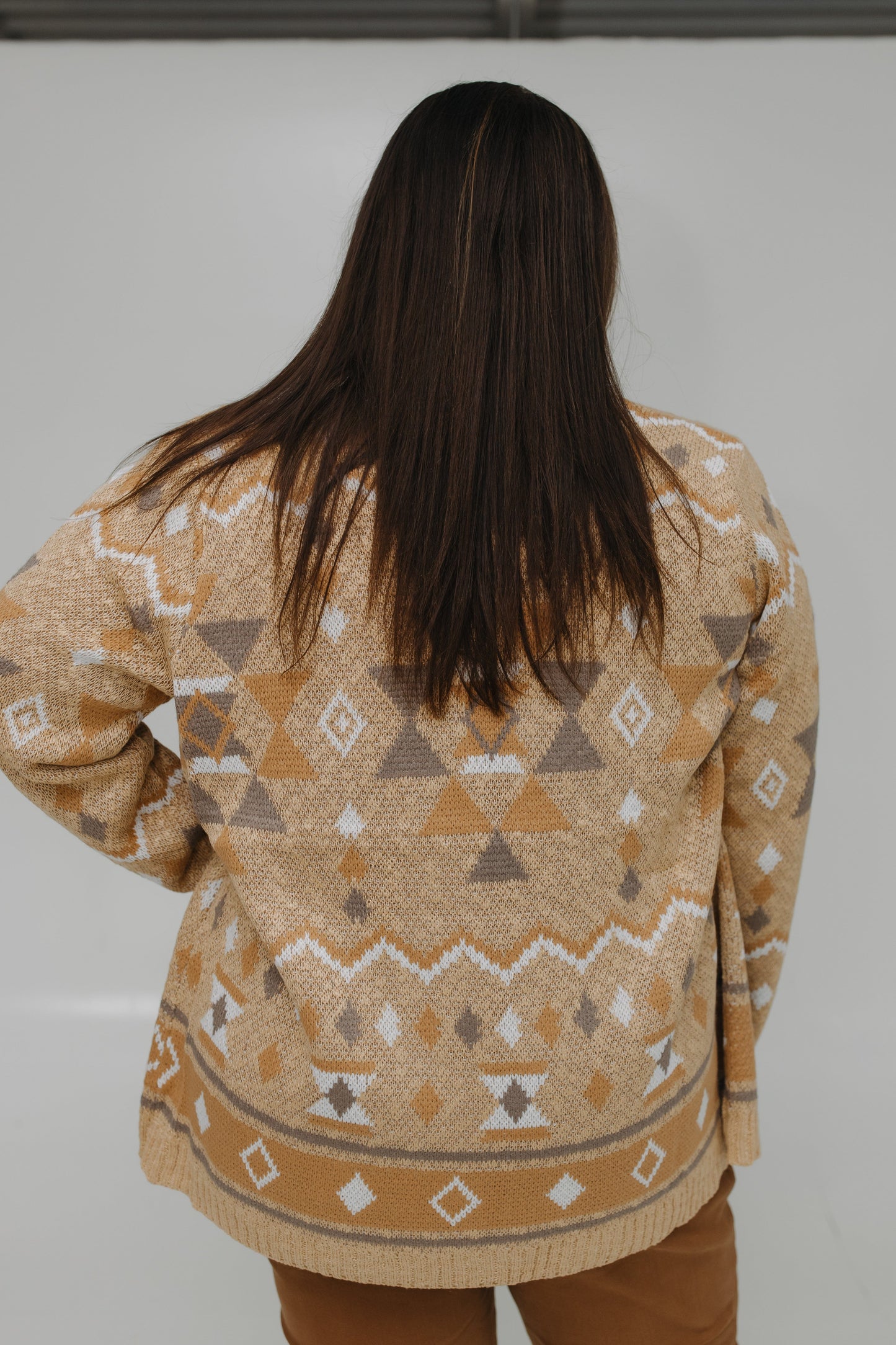 Person wearing a patterned beige sweater against a white background