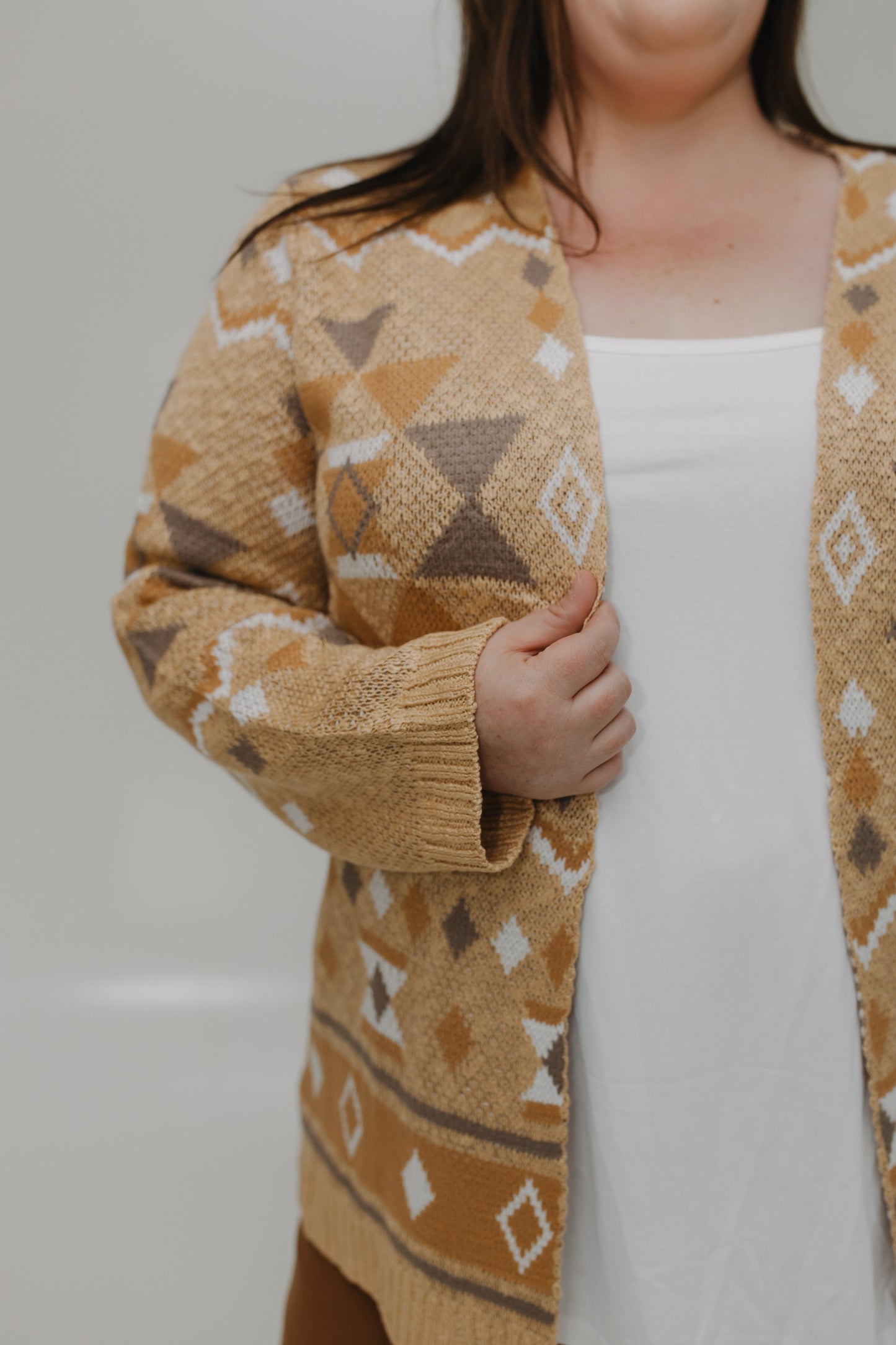 Person wearing a patterned beige cardigan over a white dress against a plain background