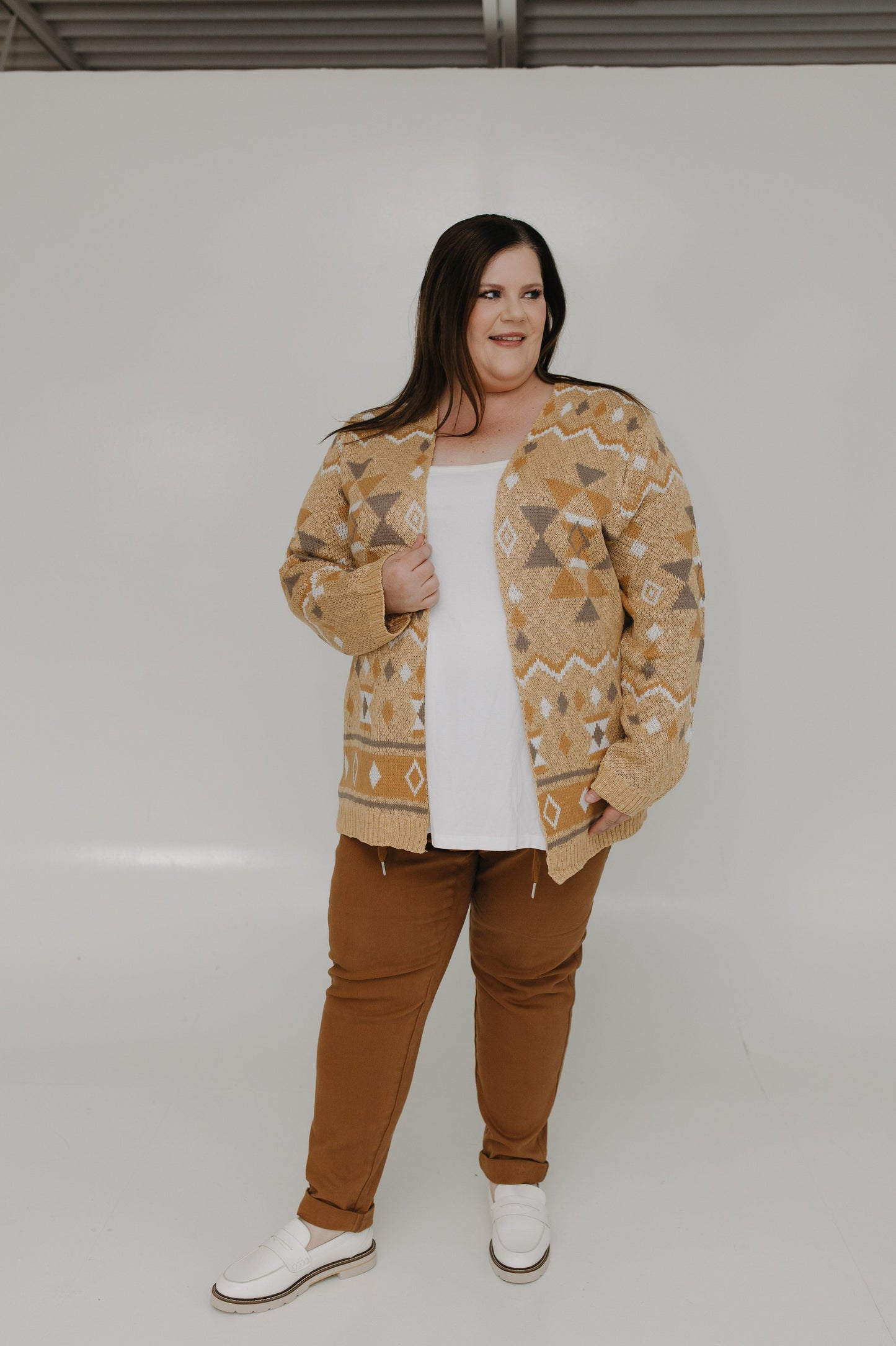 Person wearing a patterned jacket and brown pants on a white background