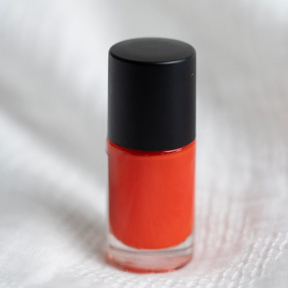 Orange nail polish with black cap on a white background
