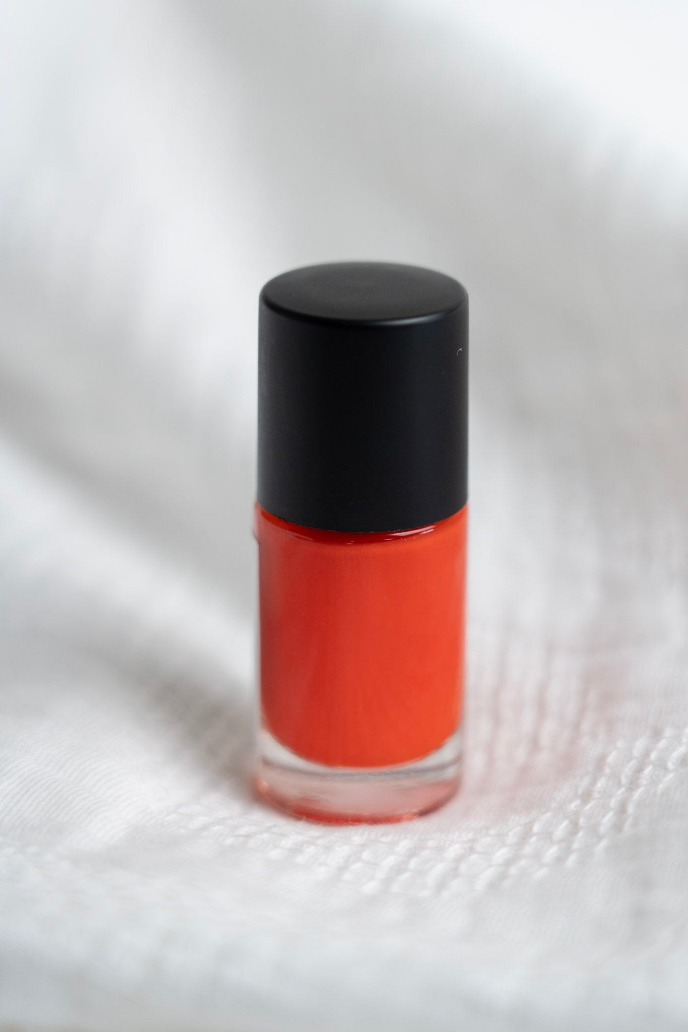 Orange nail polish with black cap on a white background