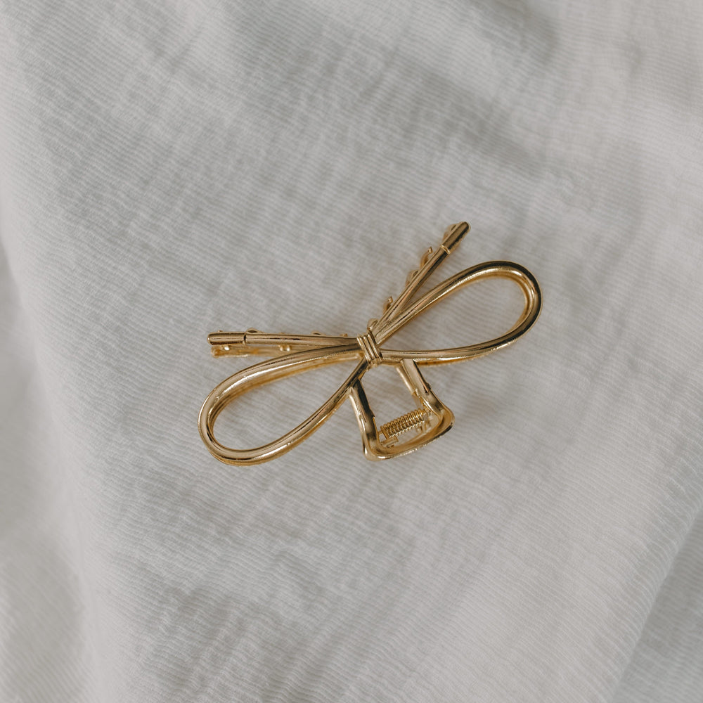 Gold bow-shaped hair clip on a white fabric background