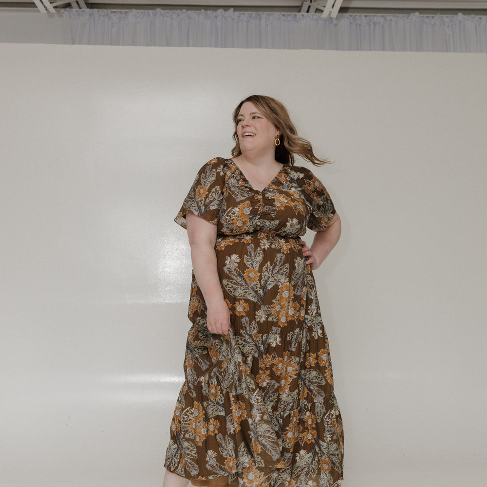 Woman wearing a floral dress standing against a plain white wall.
