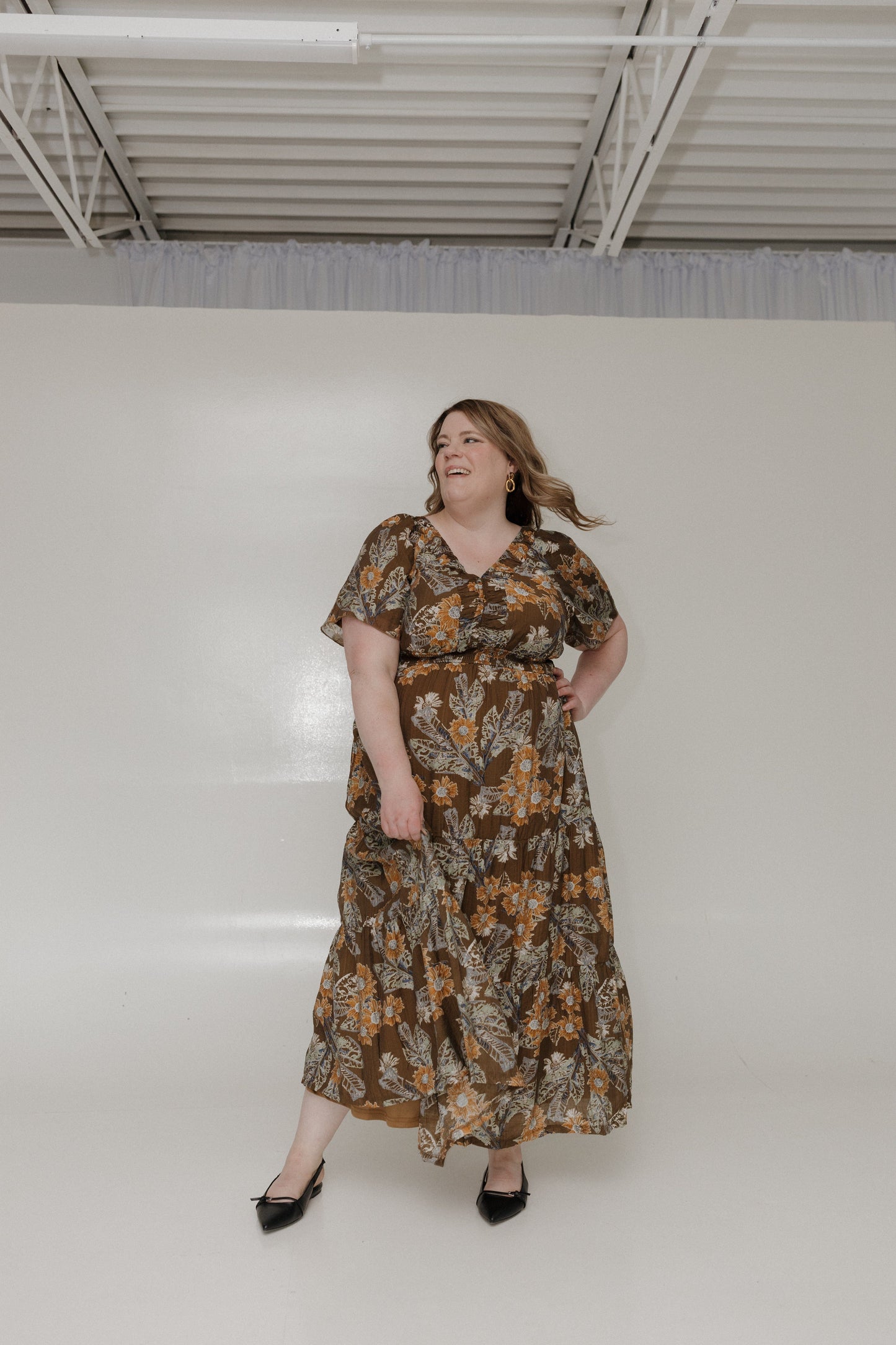 Woman wearing a floral dress standing against a plain white wall.