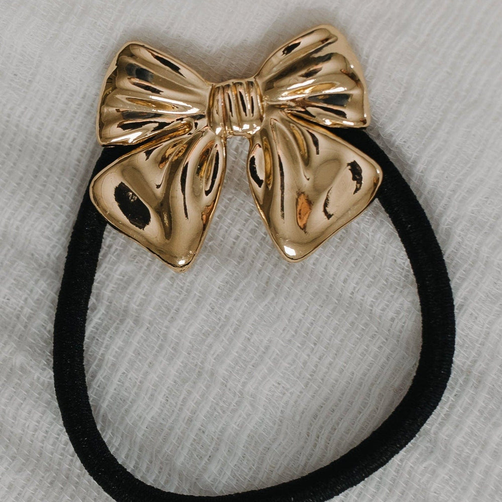 Gold bow hair tie on a gray background