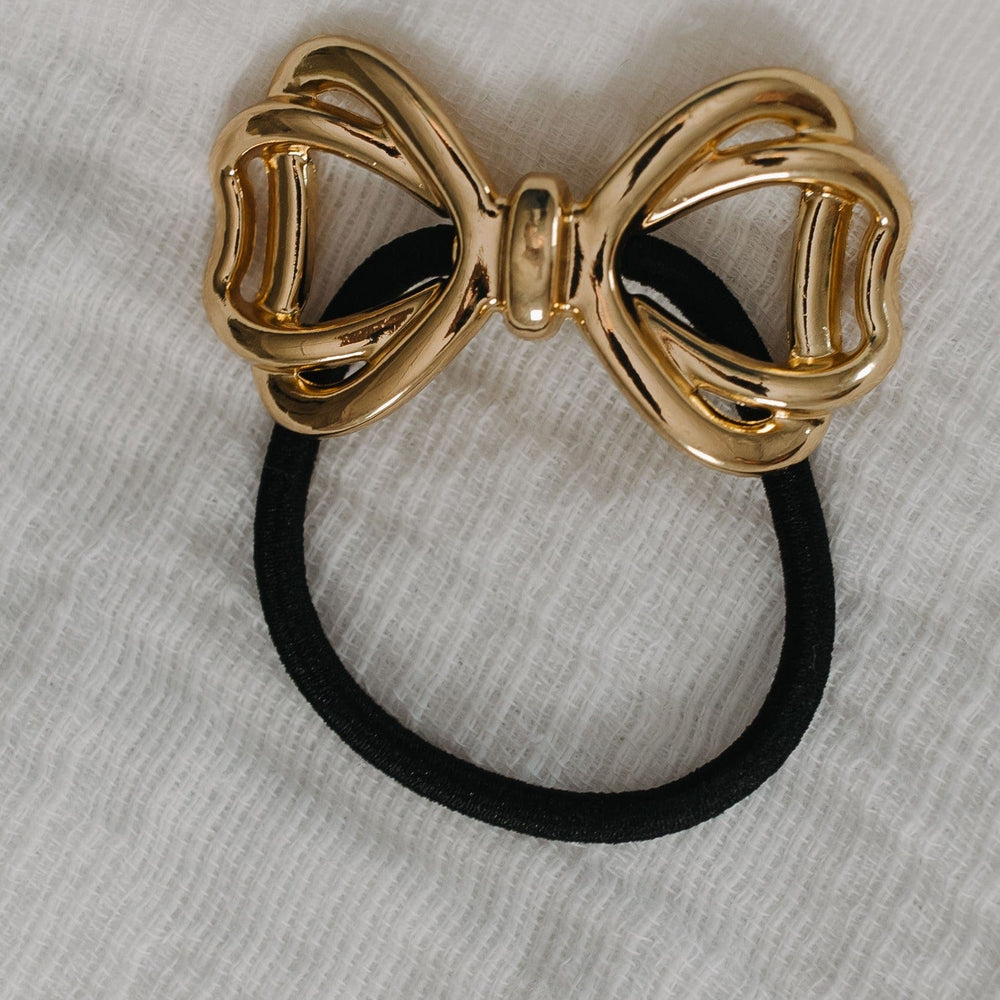 Gold bow-shaped hair tie on a gray background