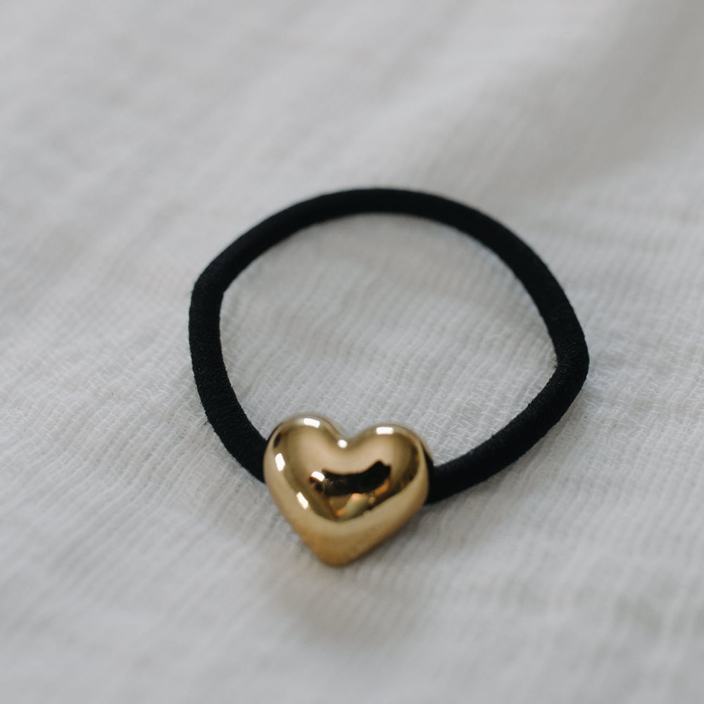Black hair tie with a gold heart-shaped charm on a light gray background