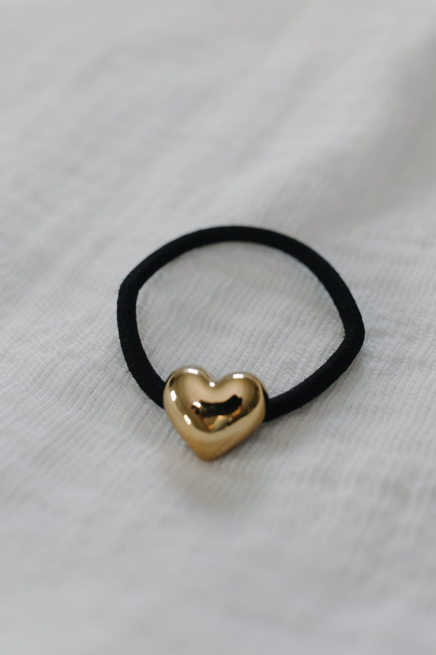 Black hair tie with a gold heart-shaped charm on a light gray background