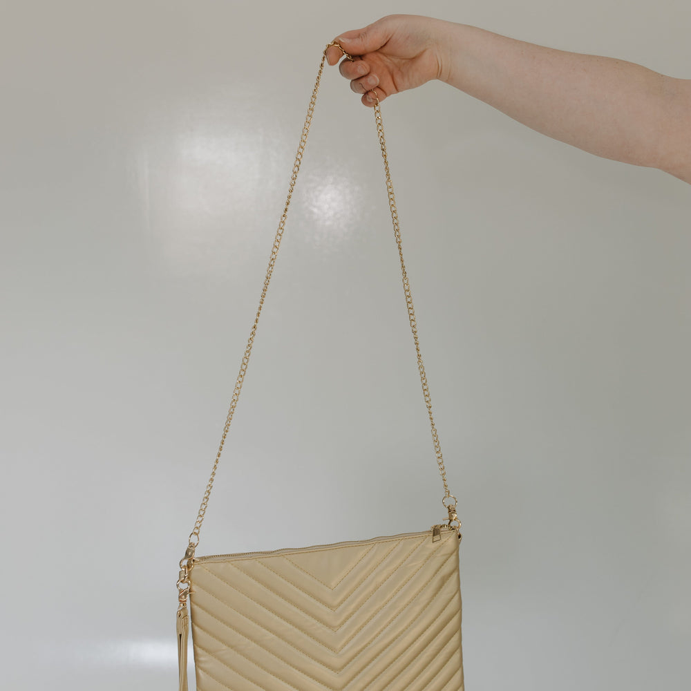 Beige handbag with a chain strap held by a hand against a neutral background