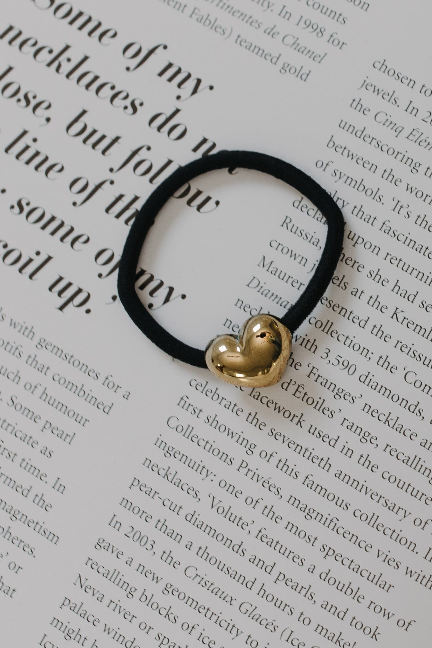 Black hair tie with a gold heart charm on a piece of paper