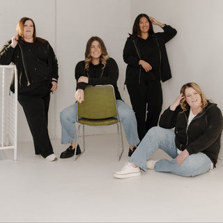 Four women posing in a minimalistic indoor setting with white walls and a white ceiling.