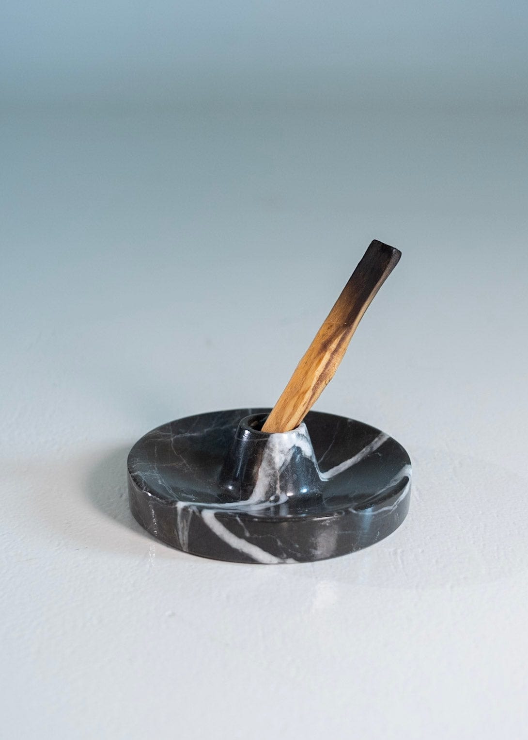 Black marble incense holder with a wooden stick on a light gray background