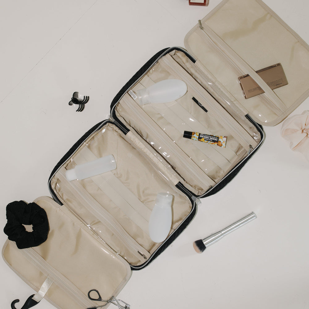 Open beige toiletry bag with various travel items on a light background