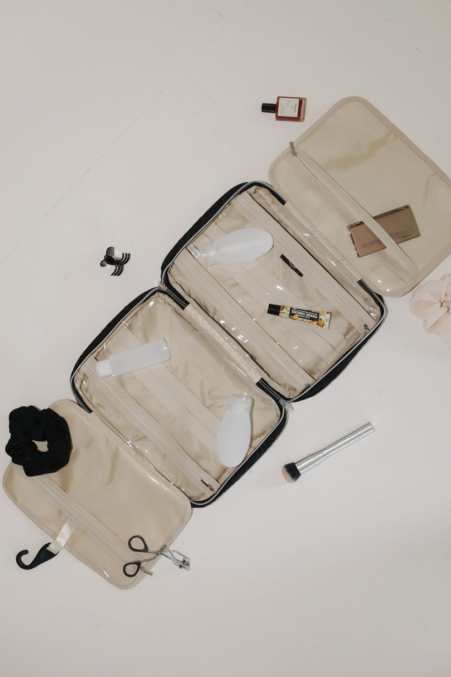 Open beige toiletry bag with various travel items on a light background