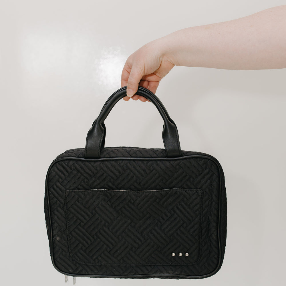 Black quilted handbag held by a hand against a light background