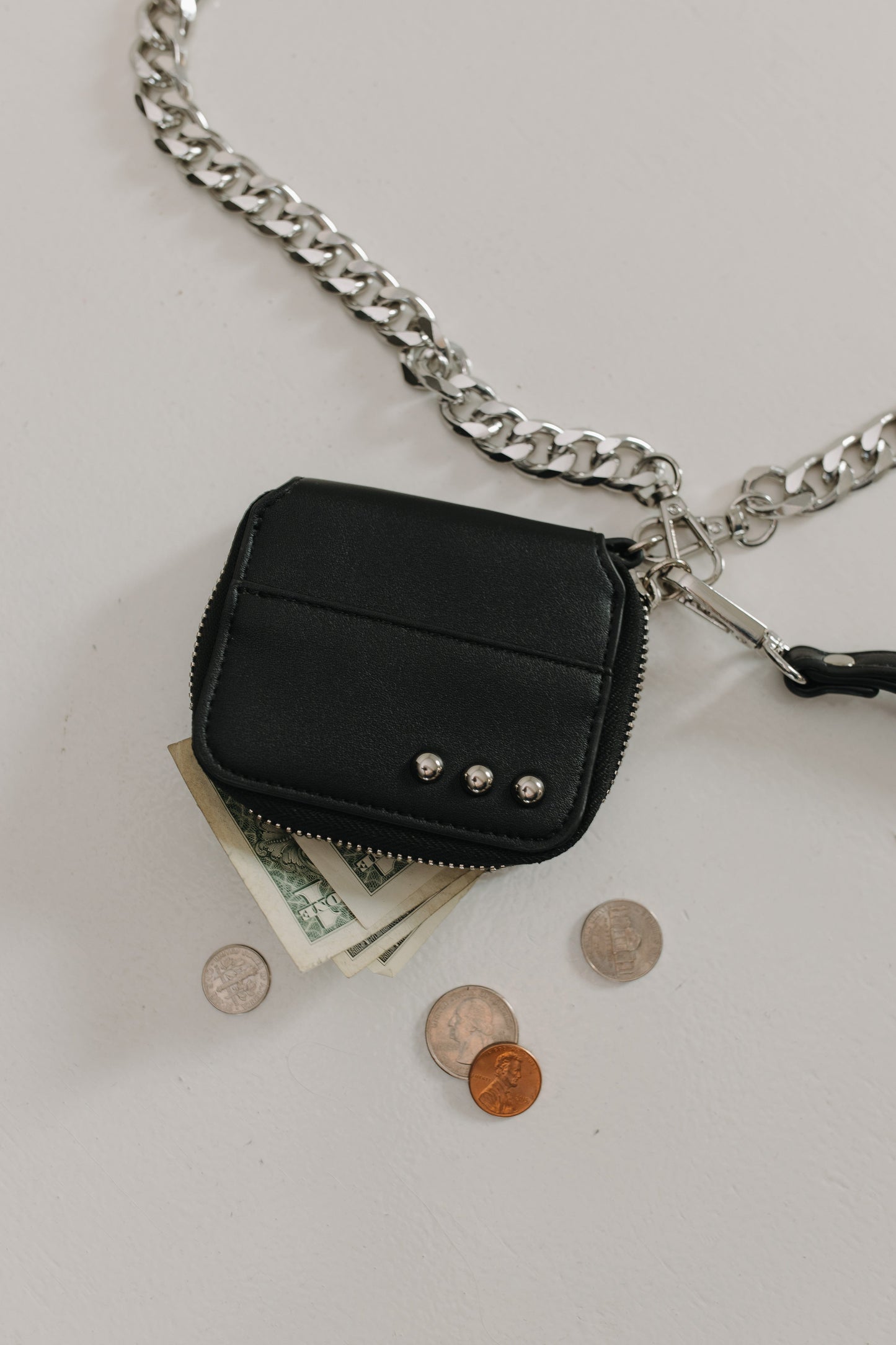 Black leather wallet with chain strap on a white background with coins and money.