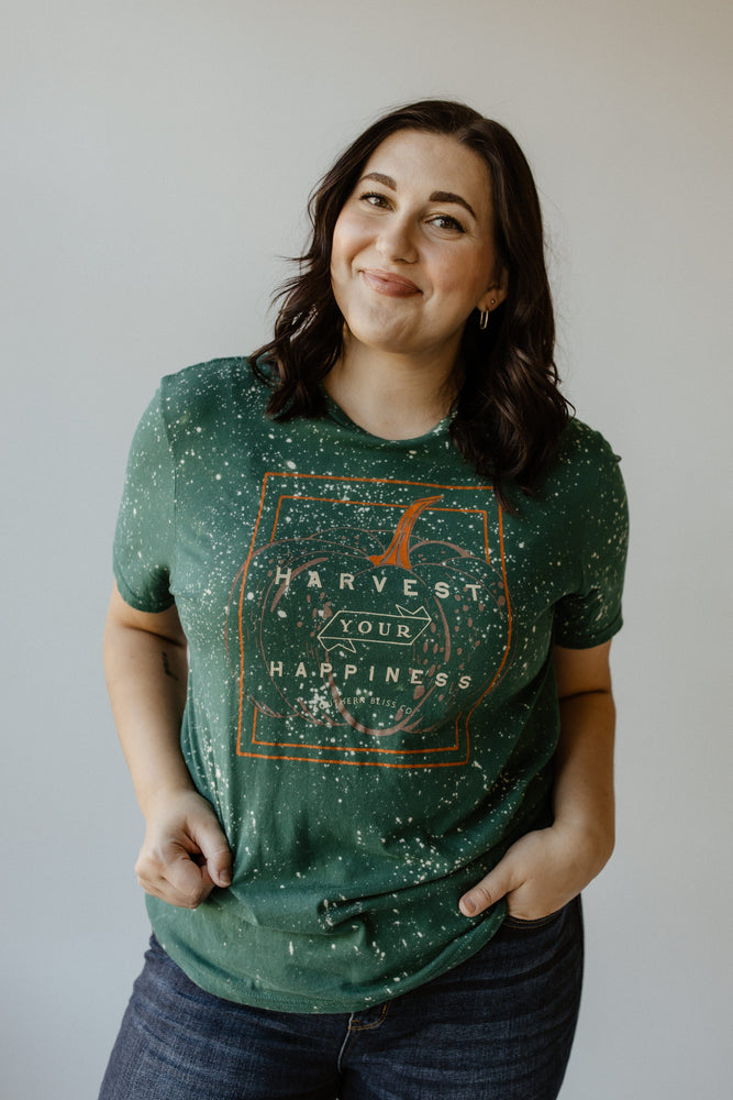 Wearing a Love Marlow "HARVEST YOUR HAPPINESS" GRAPHIC TEE in hand-bleached green, a person stands against a plain background, effortlessly highlighting fall fashion.